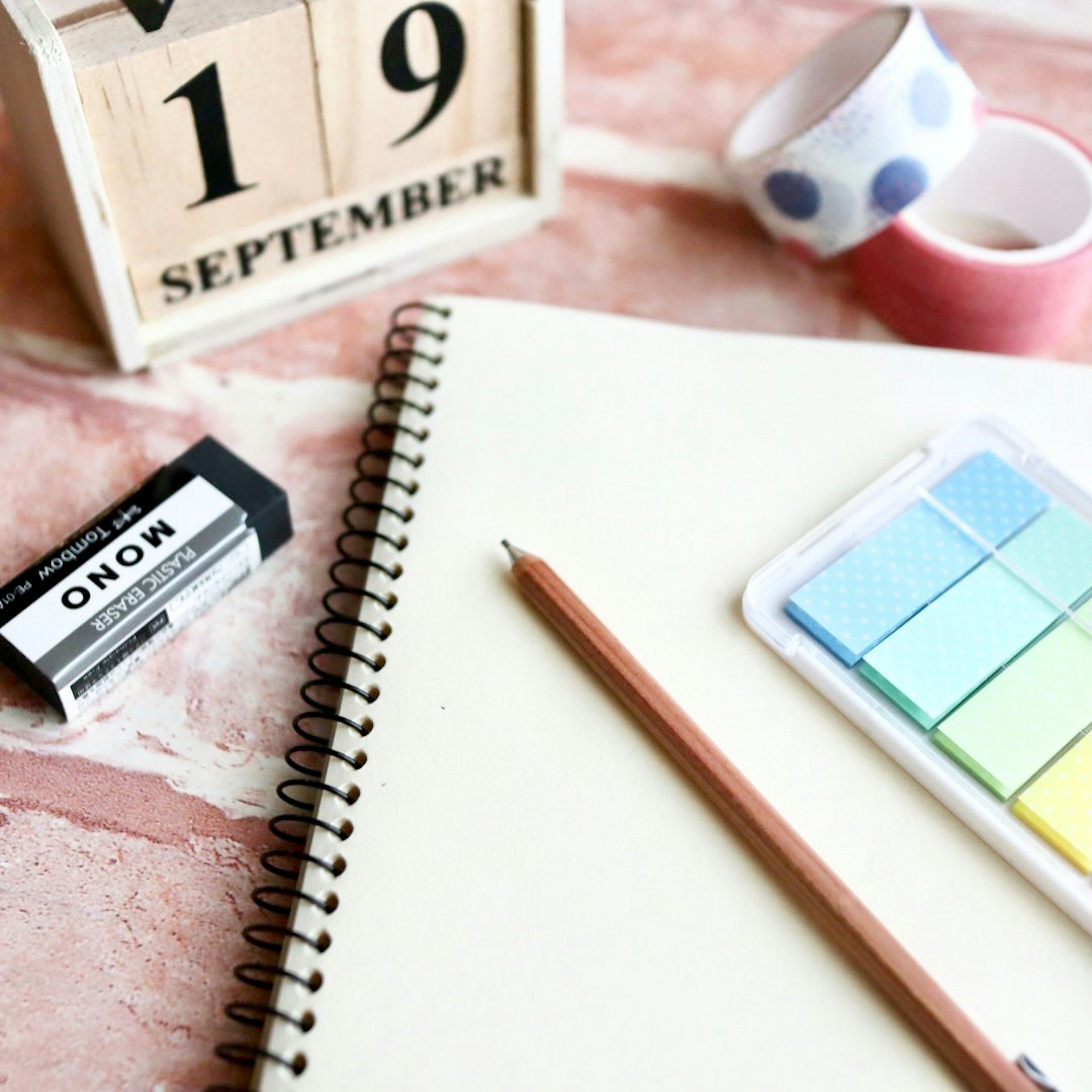 Un calendario de madera que muestra el 19 de septiembre con un cuaderno un lápiz una goma y pegatinas coloridas