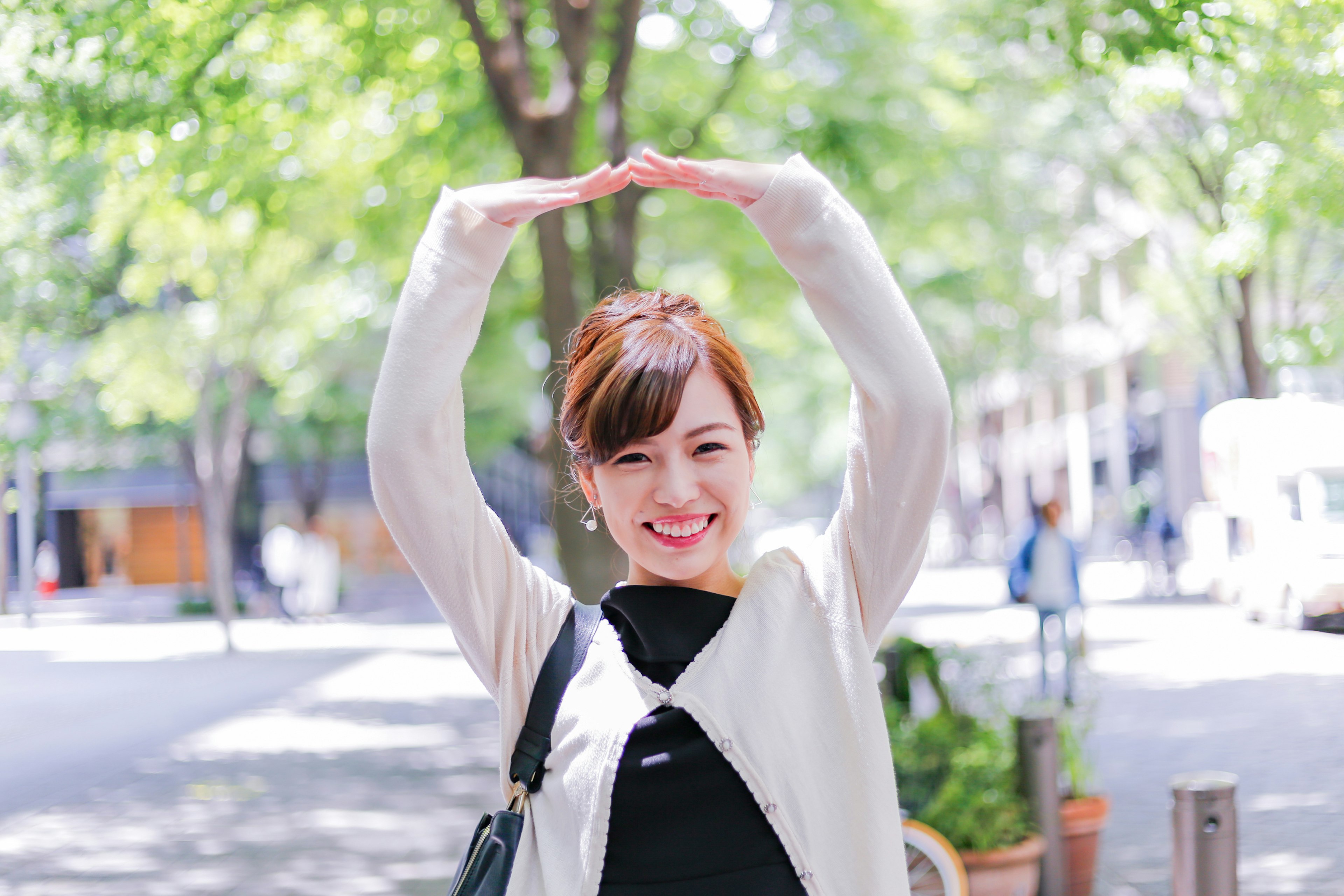 Woman posing with arms raised in a green tree-lined street