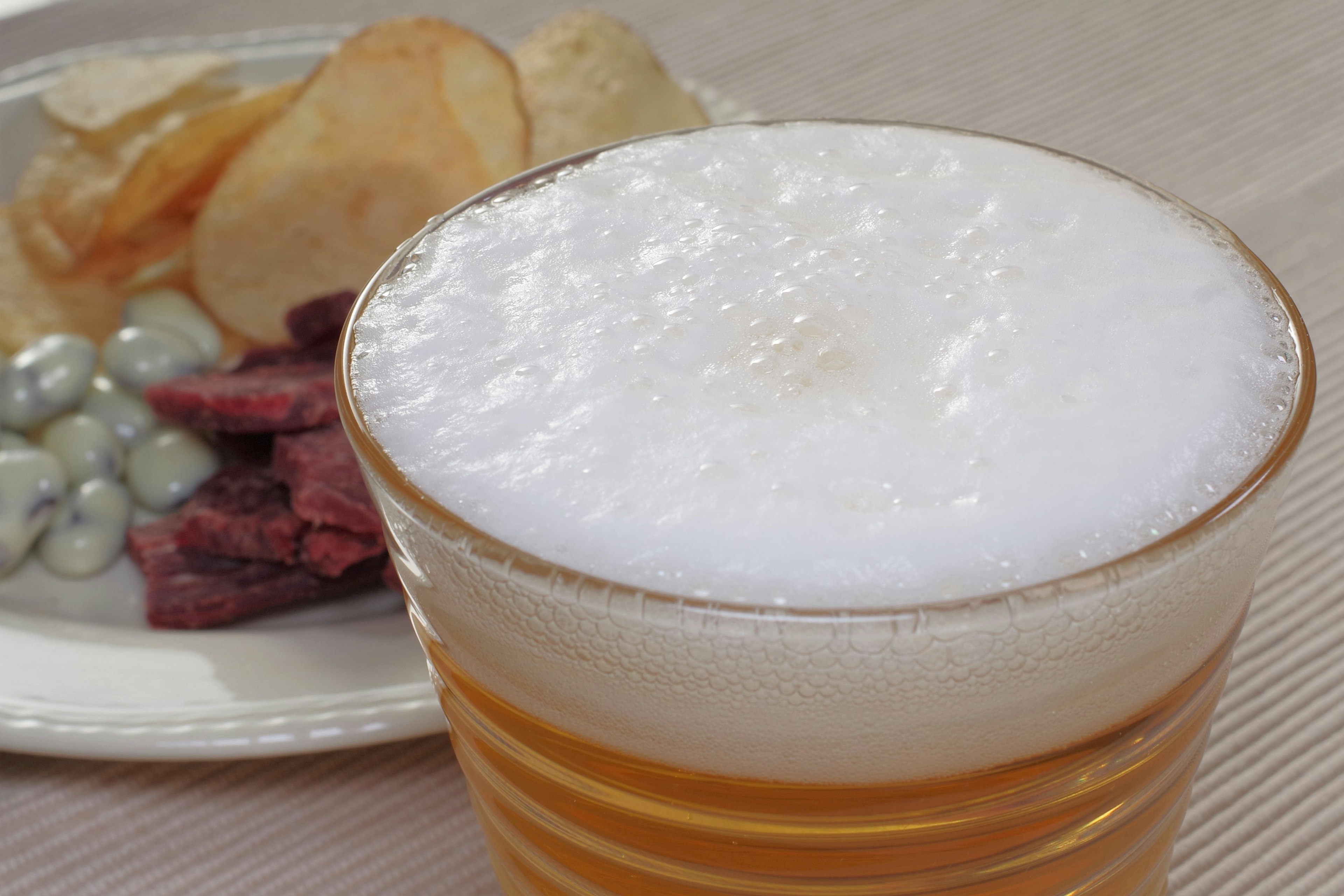 Frothy beer in a glass with snacks including chips and meat