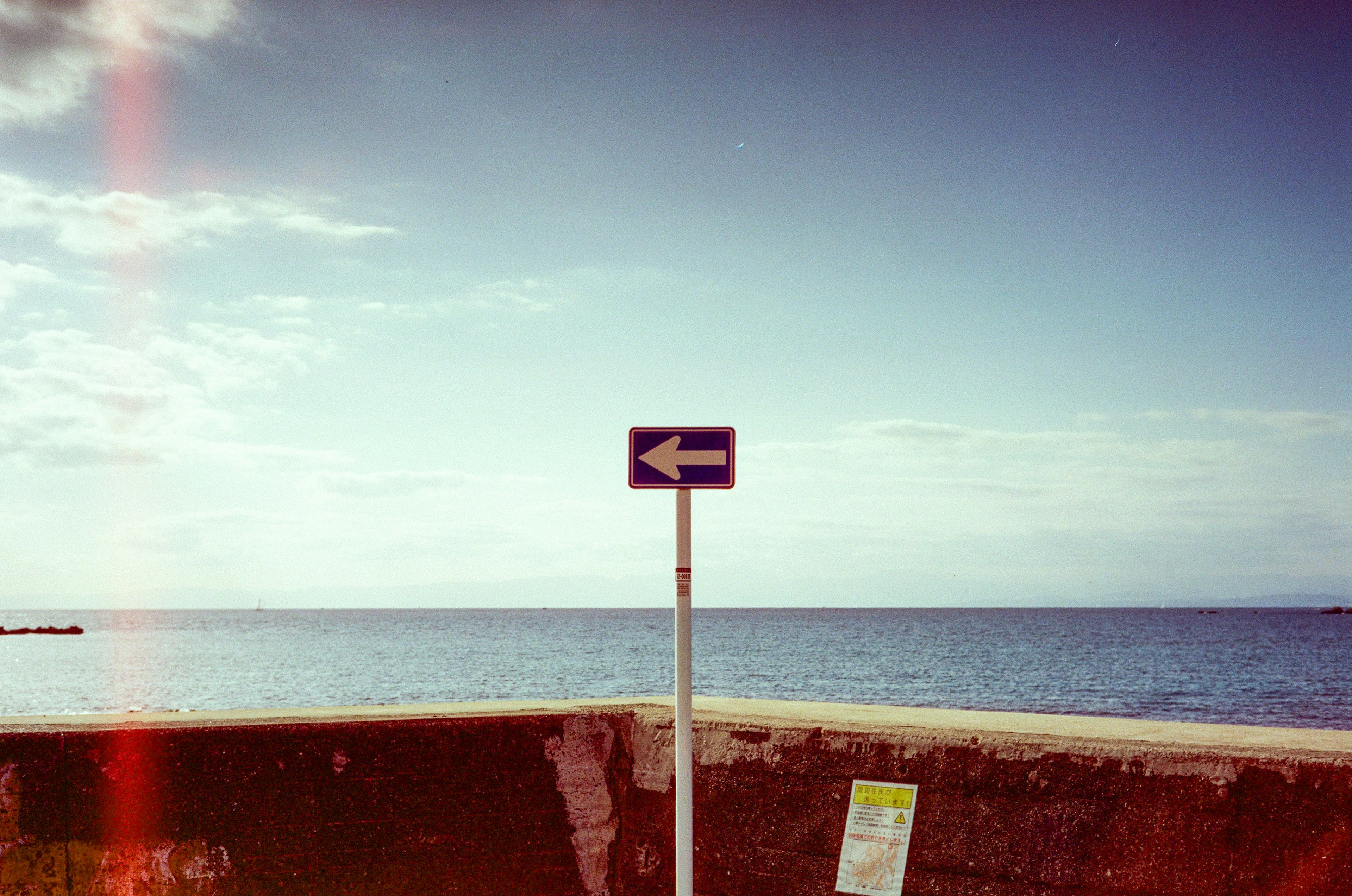 A left-facing sign near the sea with a blue sky