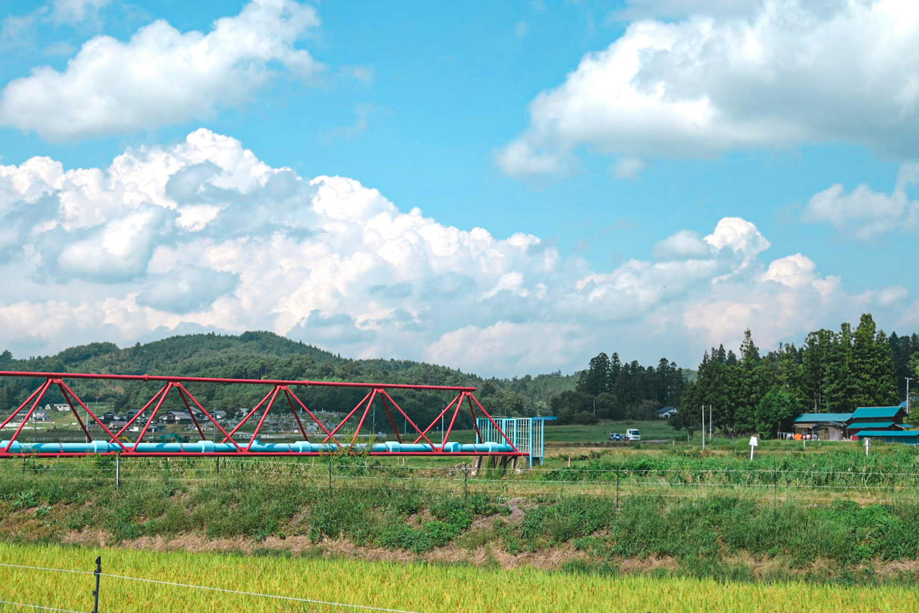 青い空と白い雲の下に赤い橋がある田舎の風景