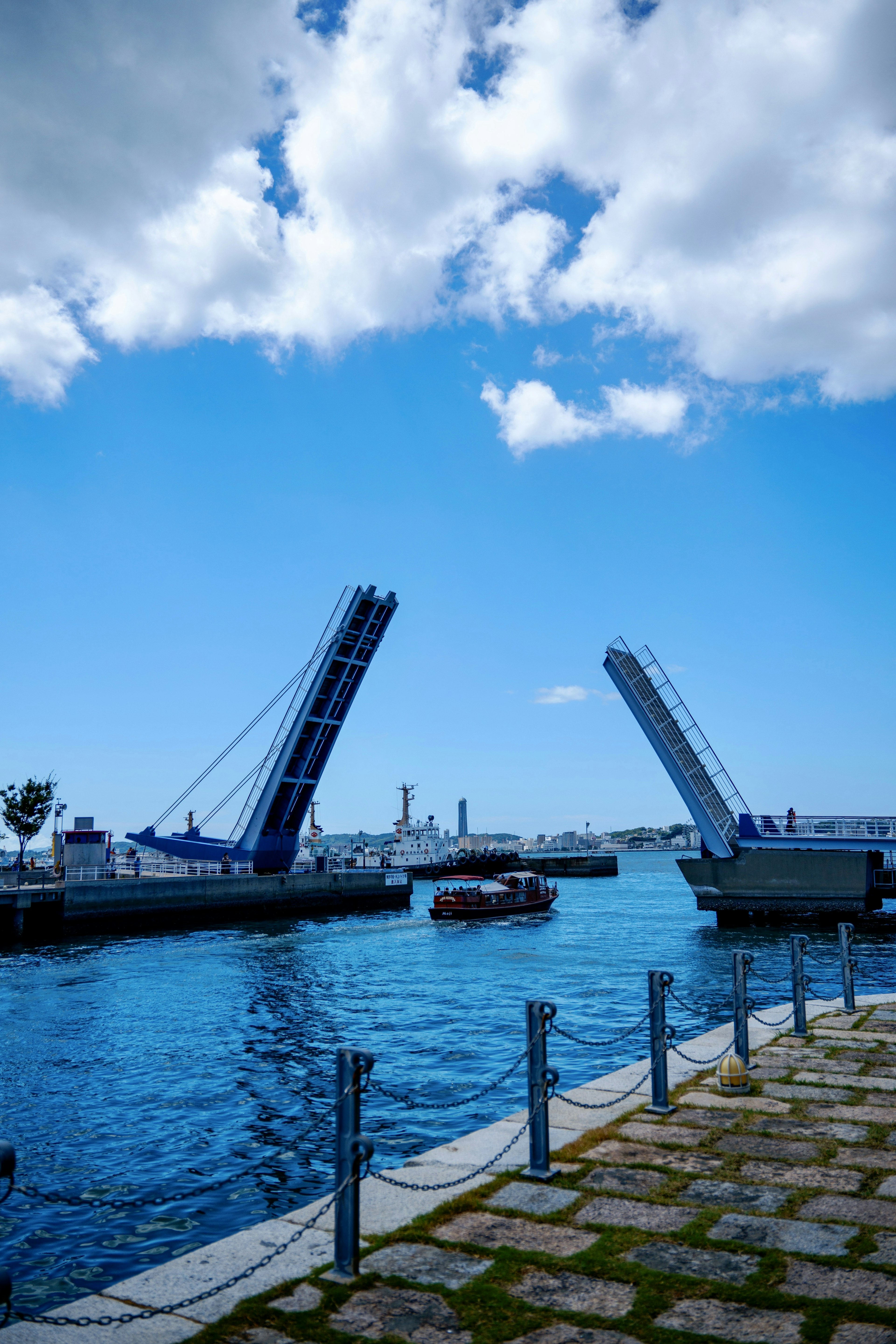 ทัศนียภาพท่าเรือที่มีสะพานยกสูงขึ้นใต้ท้องฟ้าสีฟ้า มีเรือและน้ำ