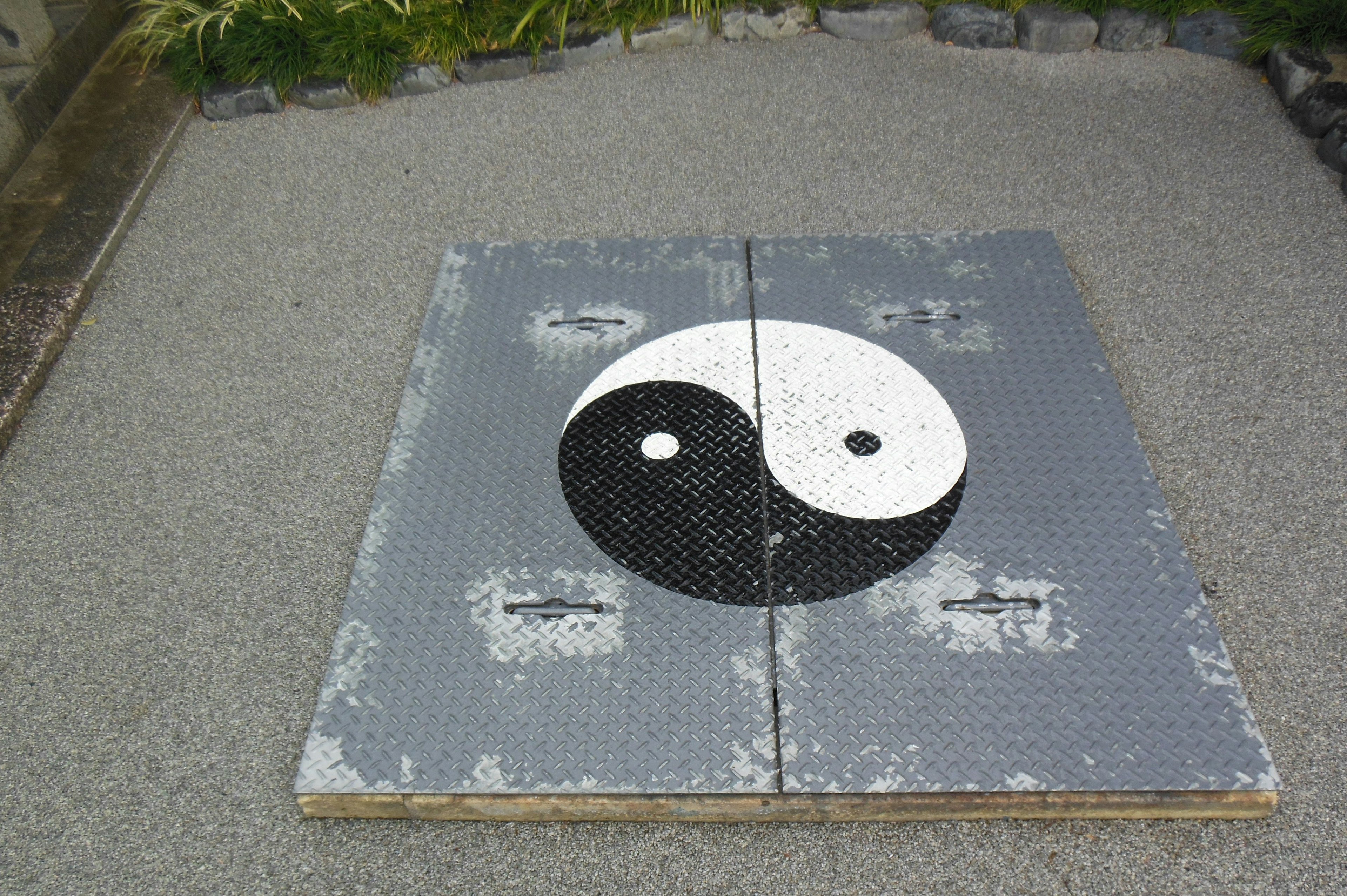 Símbolo yin yang circular en un panel de piedra texturizado rodeado de grava