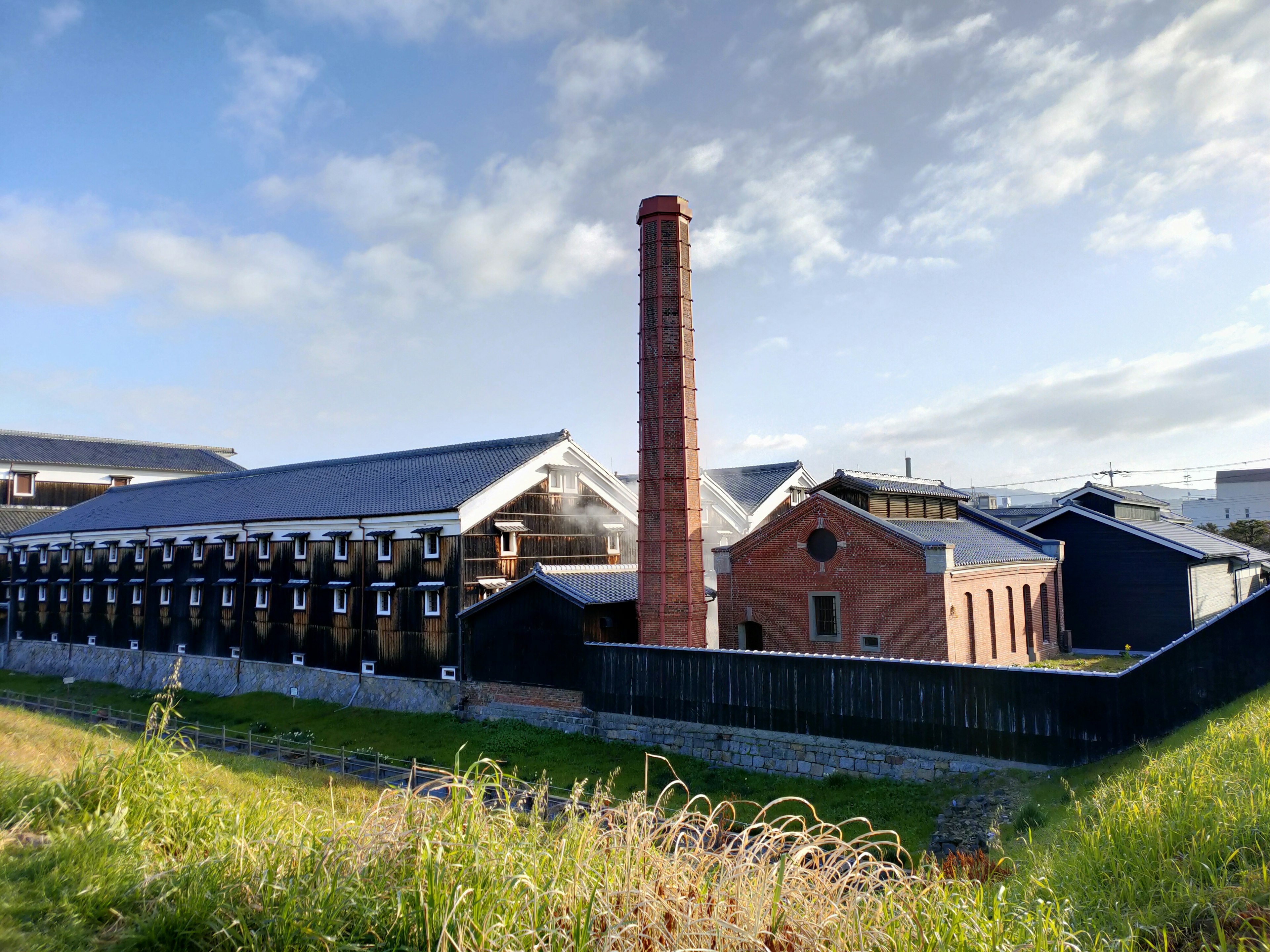 Fabrikaußenansicht mit einem roten Ziegelschornstein vor grünem Gras