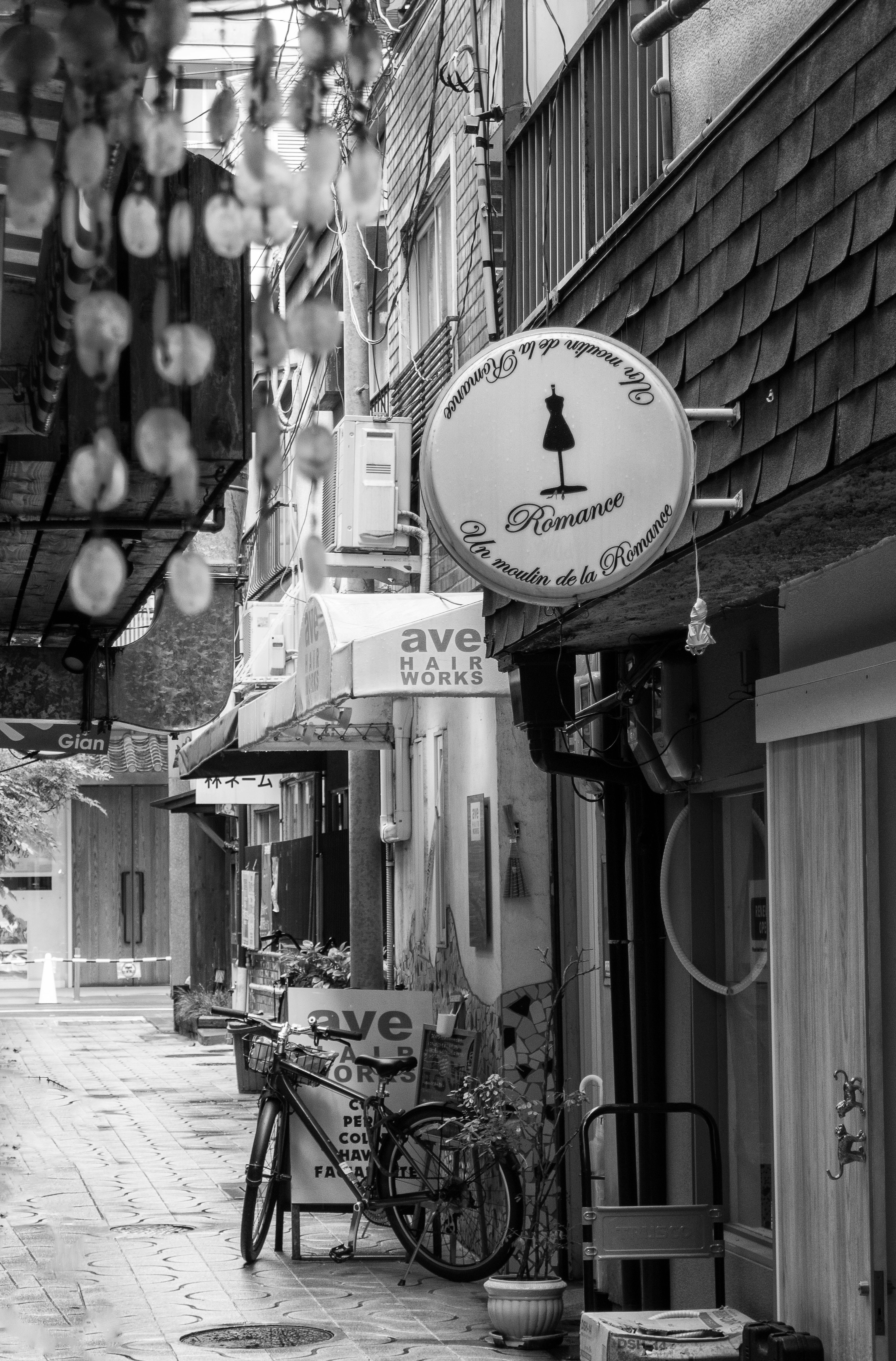 Narrow alley featuring a café sign and a bicycle in black and white