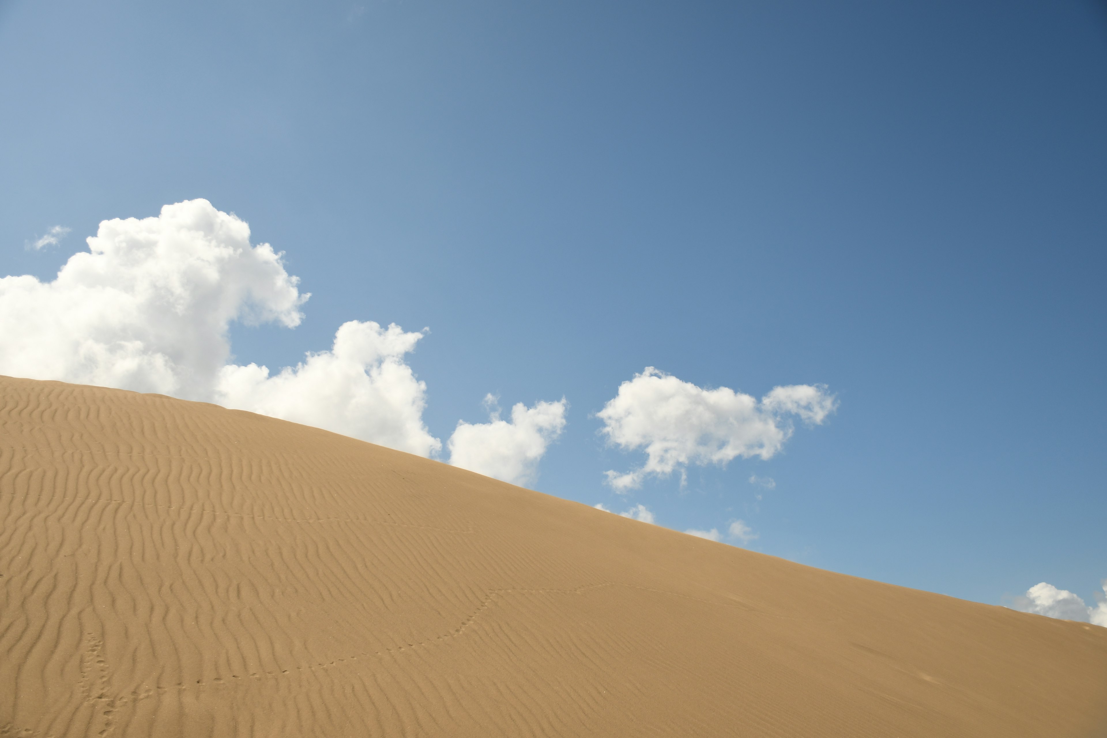 Sanddünenlandschaft unter einem blauen Himmel mit weißen Wolken