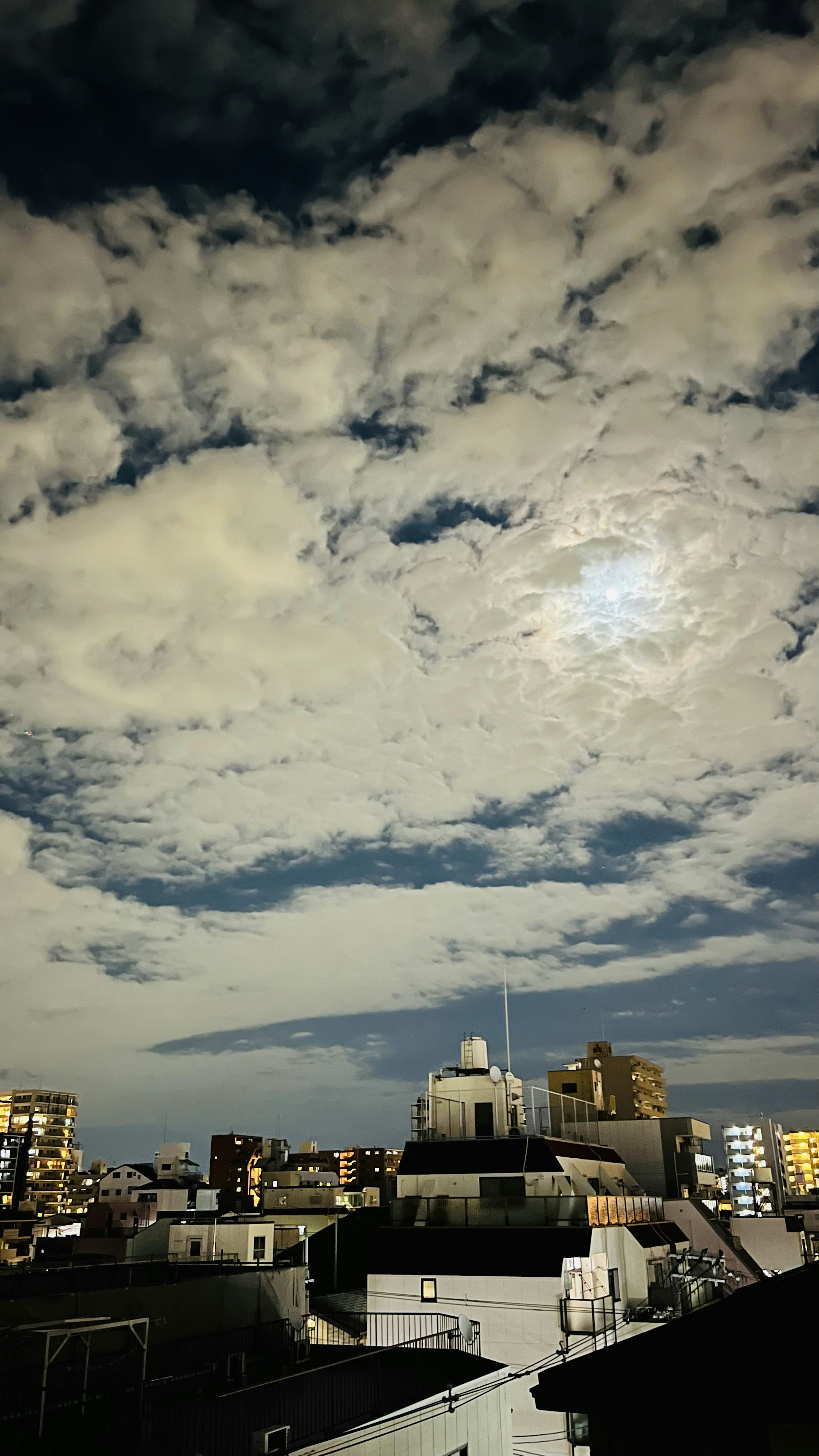 Cielo nocturno nublado con luna brillante sobre los techos de la ciudad