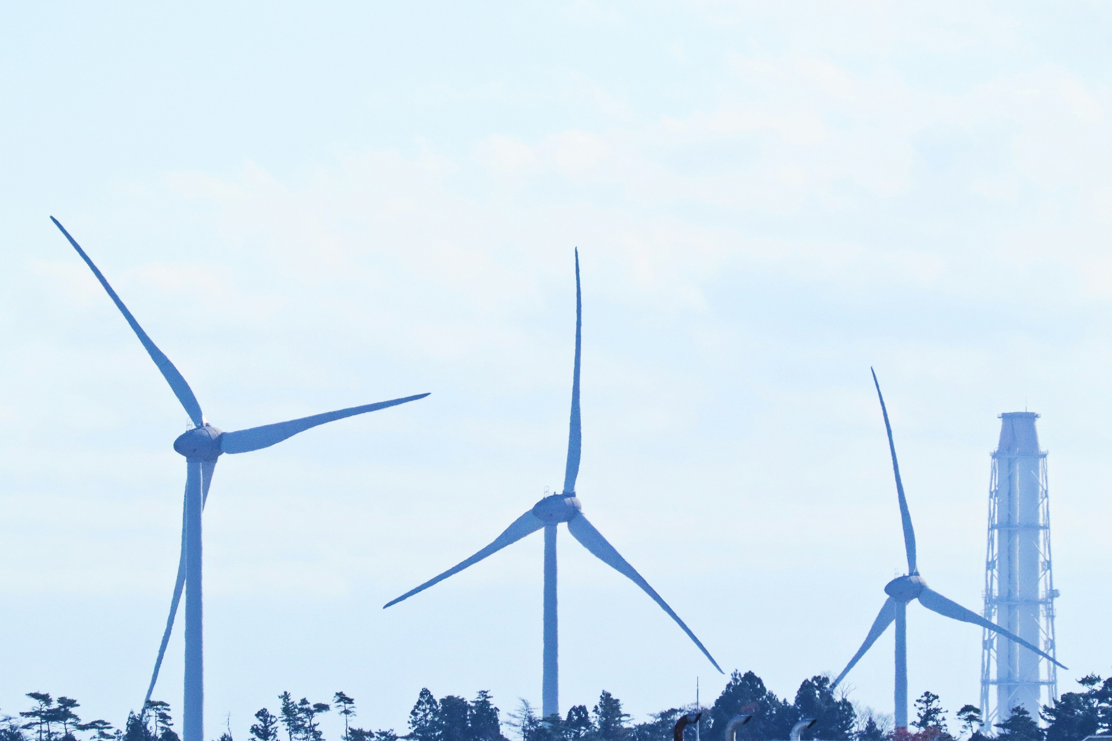 Landscape featuring wind turbines and a smokestack under a blue sky