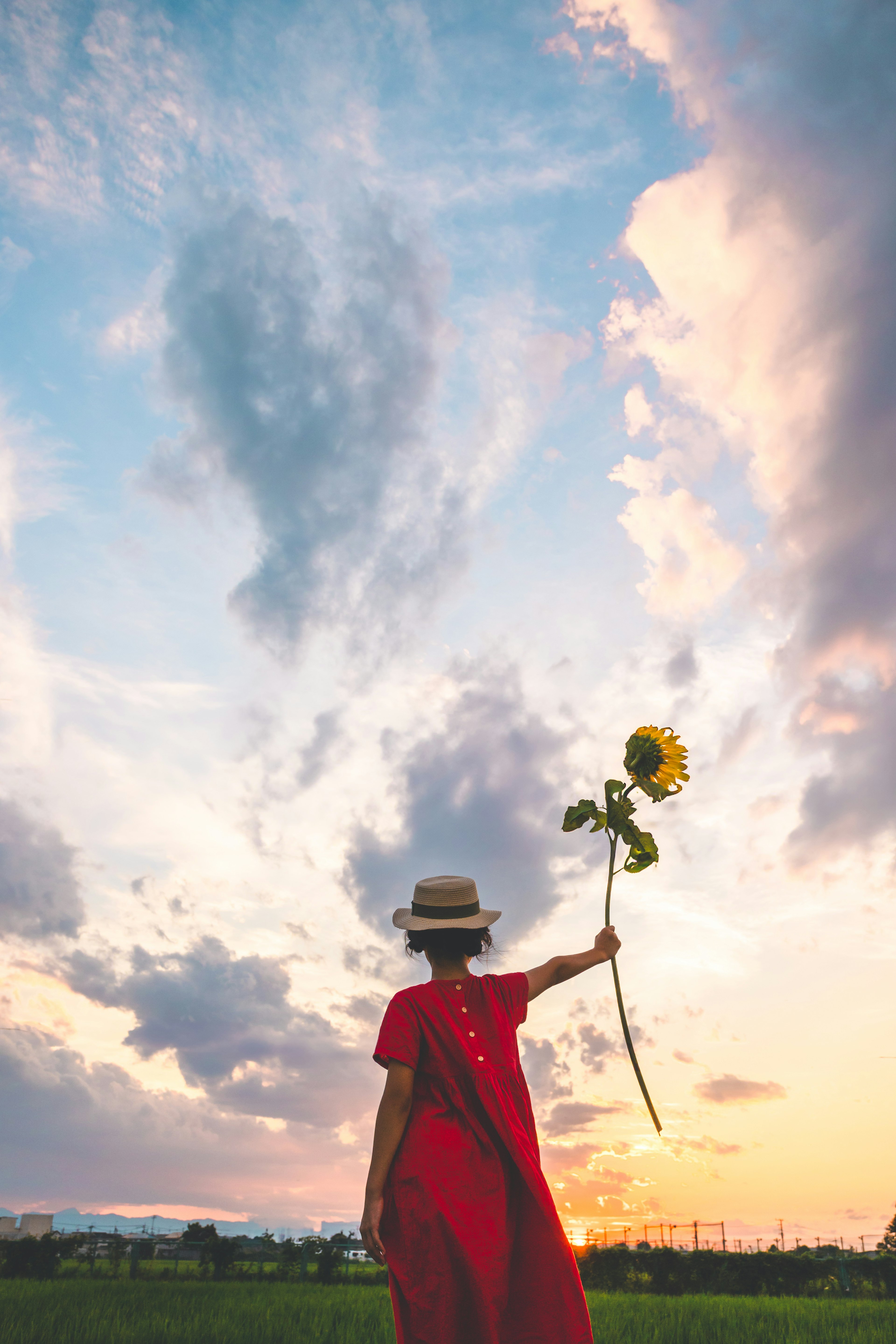 Woman in a red dress holding a sunflower looking up at the sky