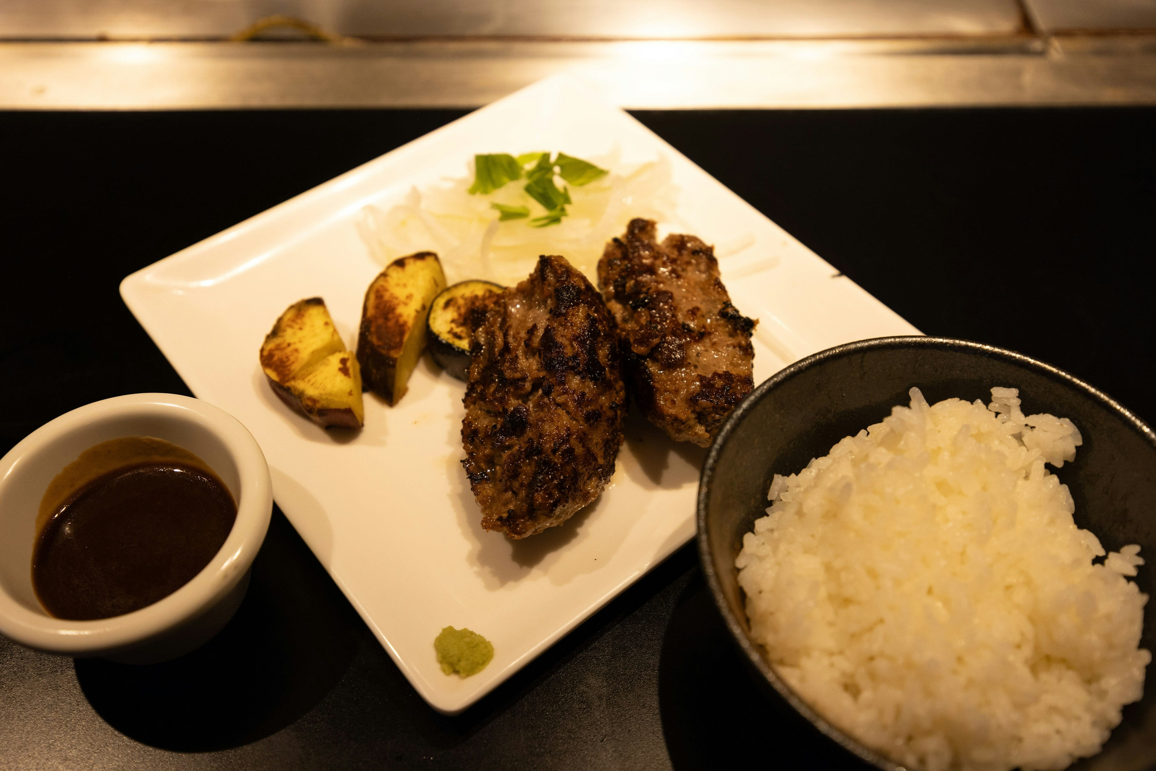 白い皿に盛り付けられた焼き肉とご飯の料理 醤油ソースと焼き野菜が添えられている