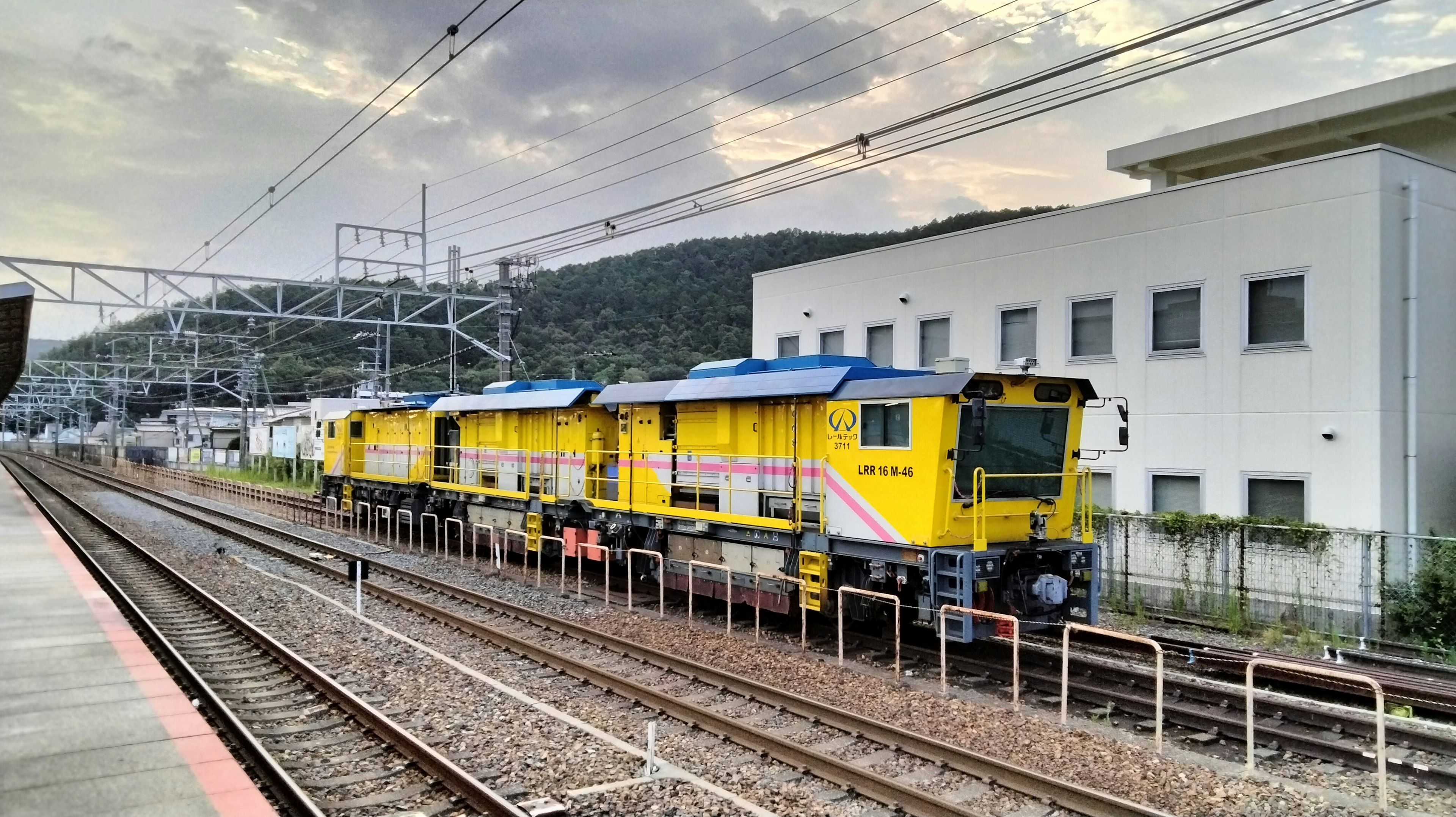 Lokomotif kuning diparkir di rel dengan bangunan di latar belakang