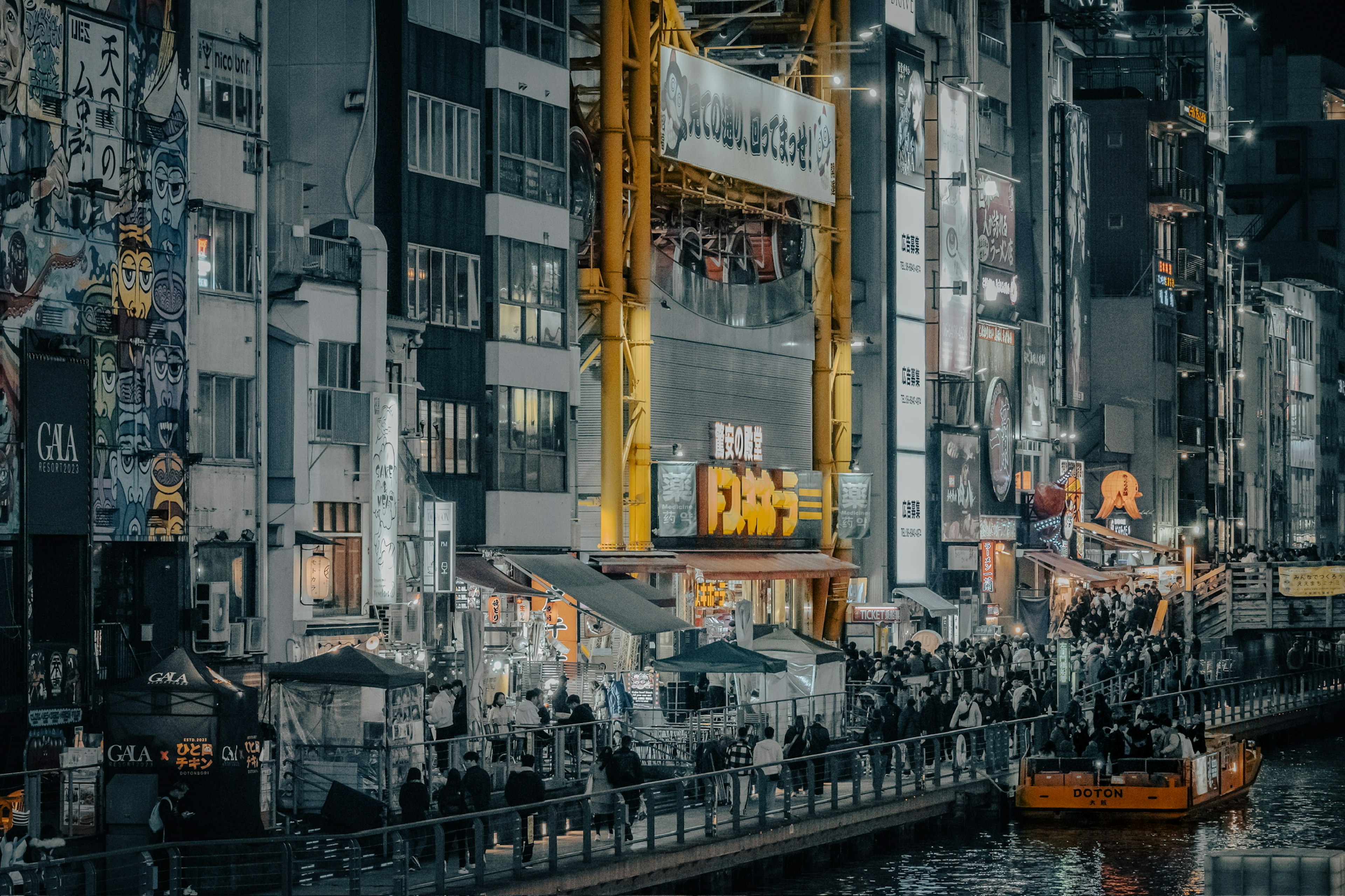 Bustling riverside stalls at night with a yellow crane in a cityscape