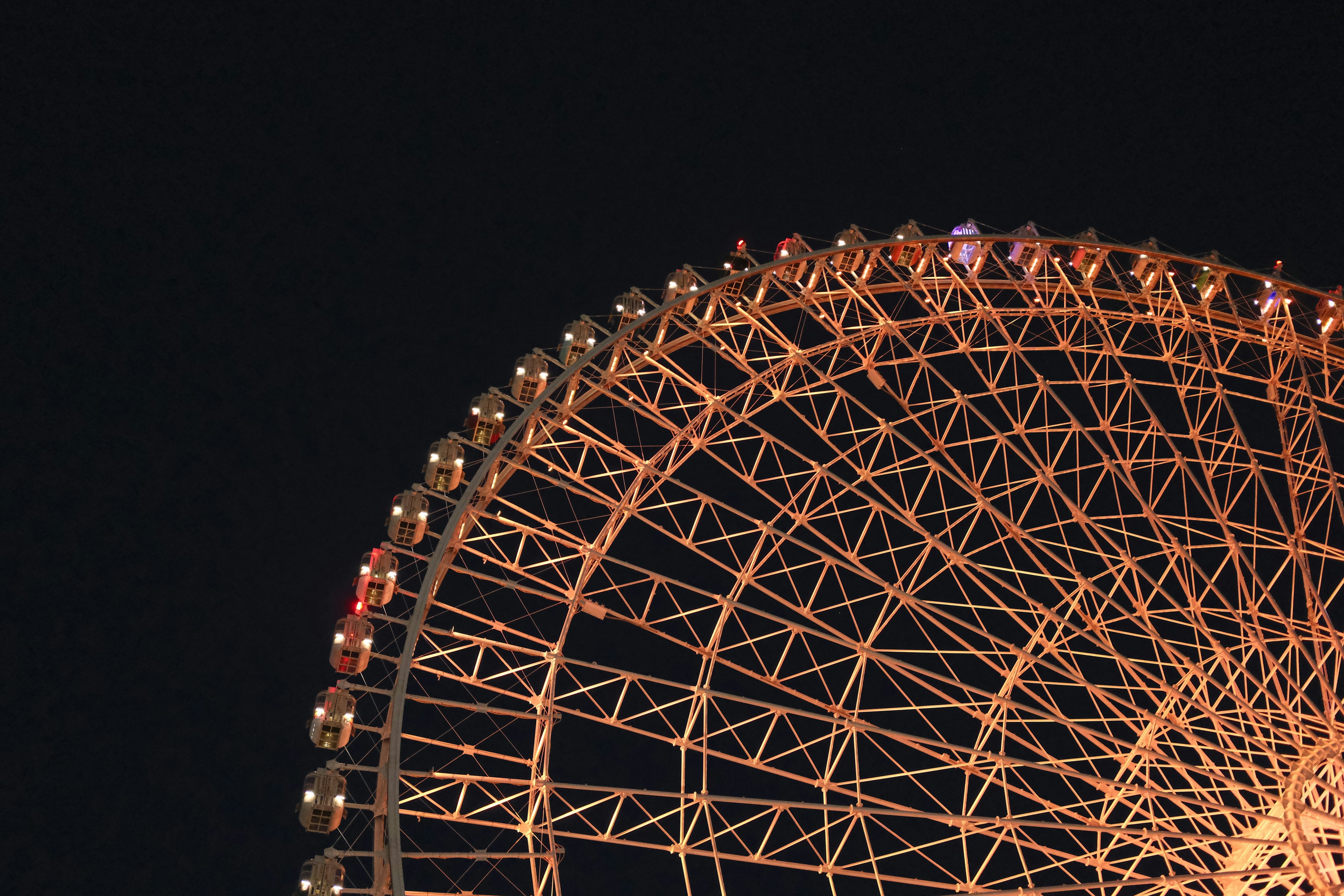 Part of a Ferris wheel illuminated against a night sky featuring vibrant orange lights