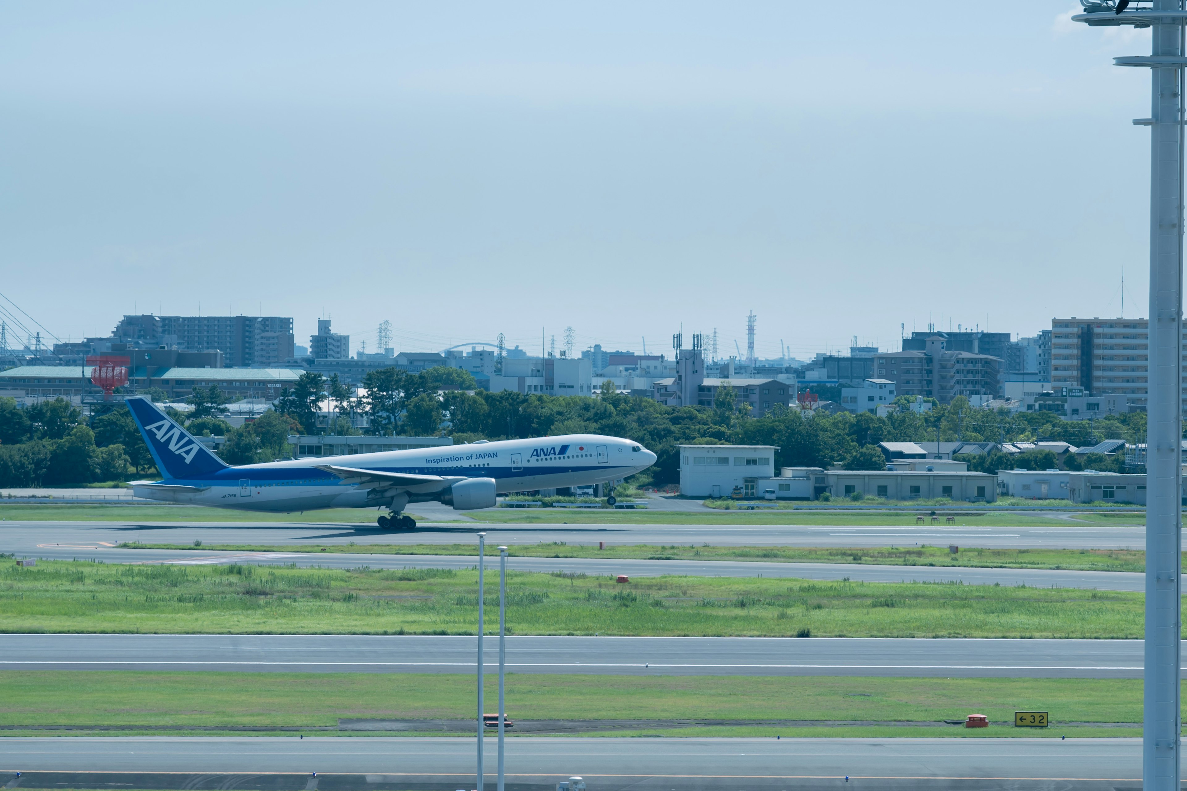 Un avión azul rodando en la pista con edificios y césped verde al fondo