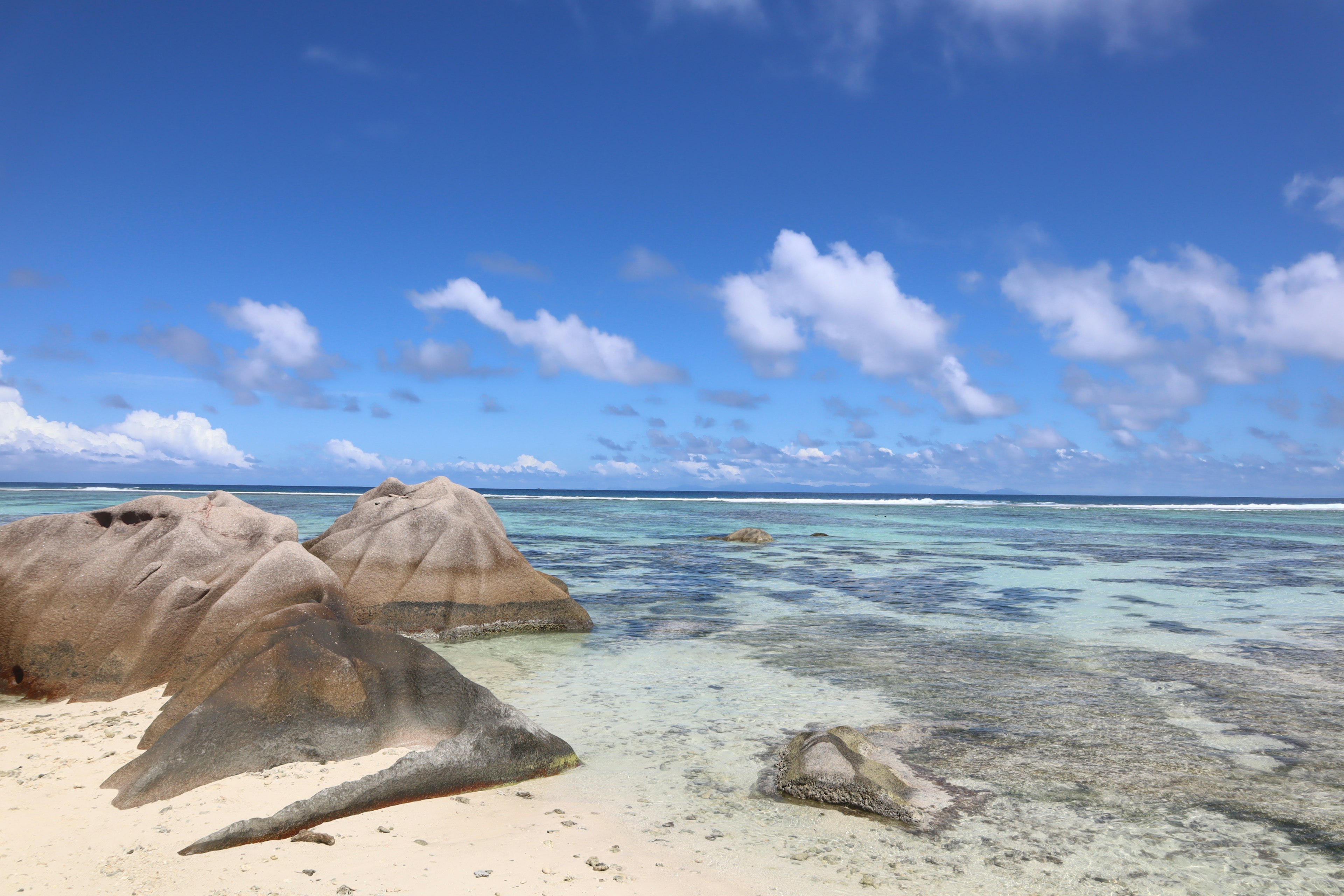 Pemandangan pantai dengan langit biru dan awan putih menampilkan batu dan air jernih