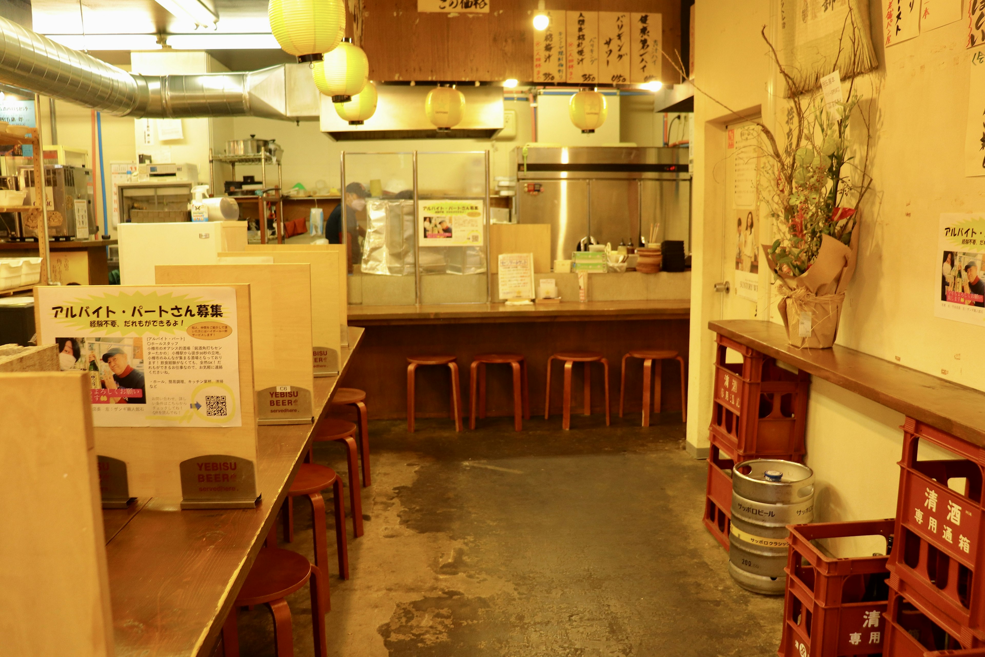 Interior of an izakaya wooden counter and chairs visible kitchen area warm lighting