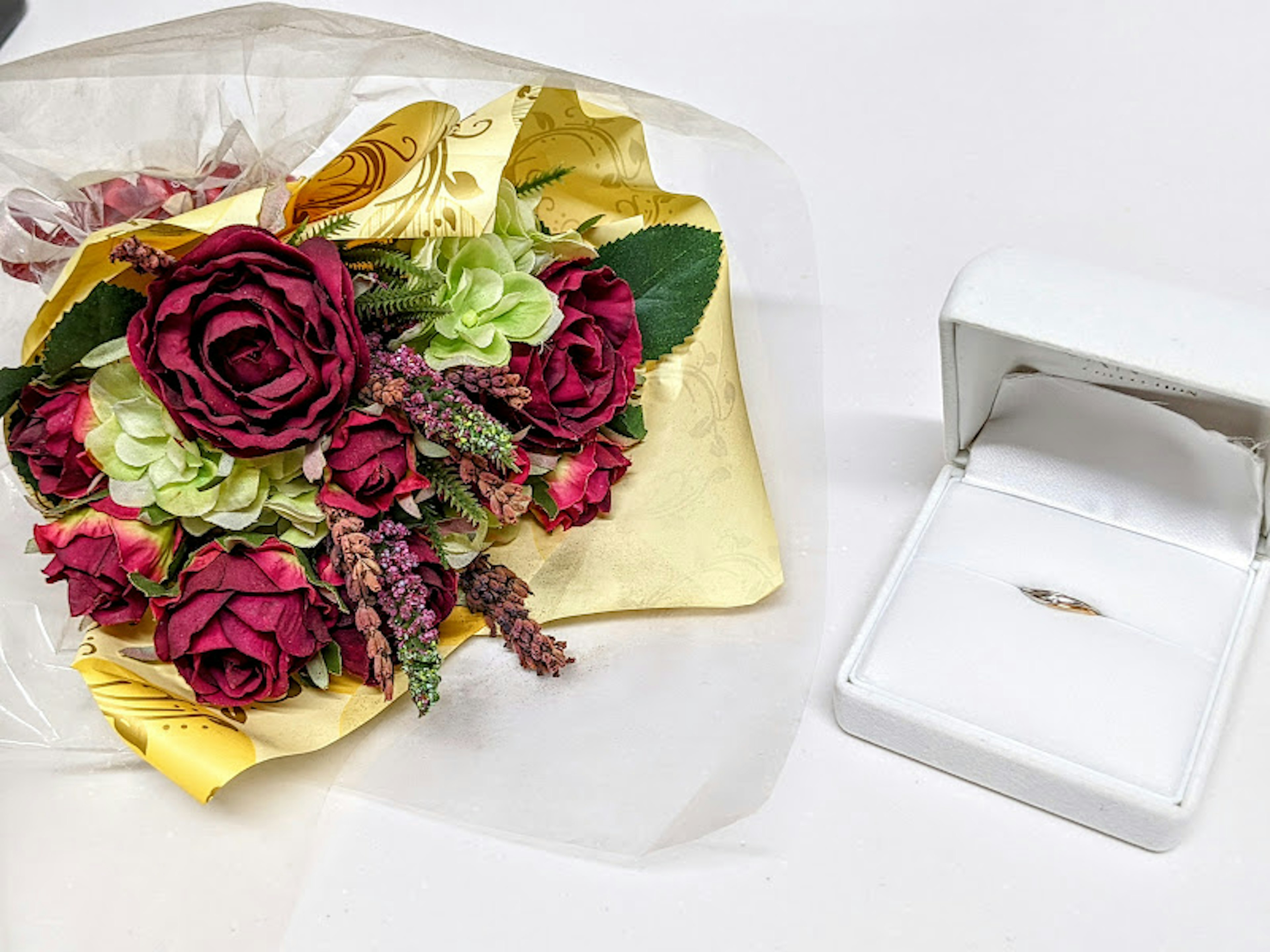 Bouquet of red roses and green flowers next to a white ring box