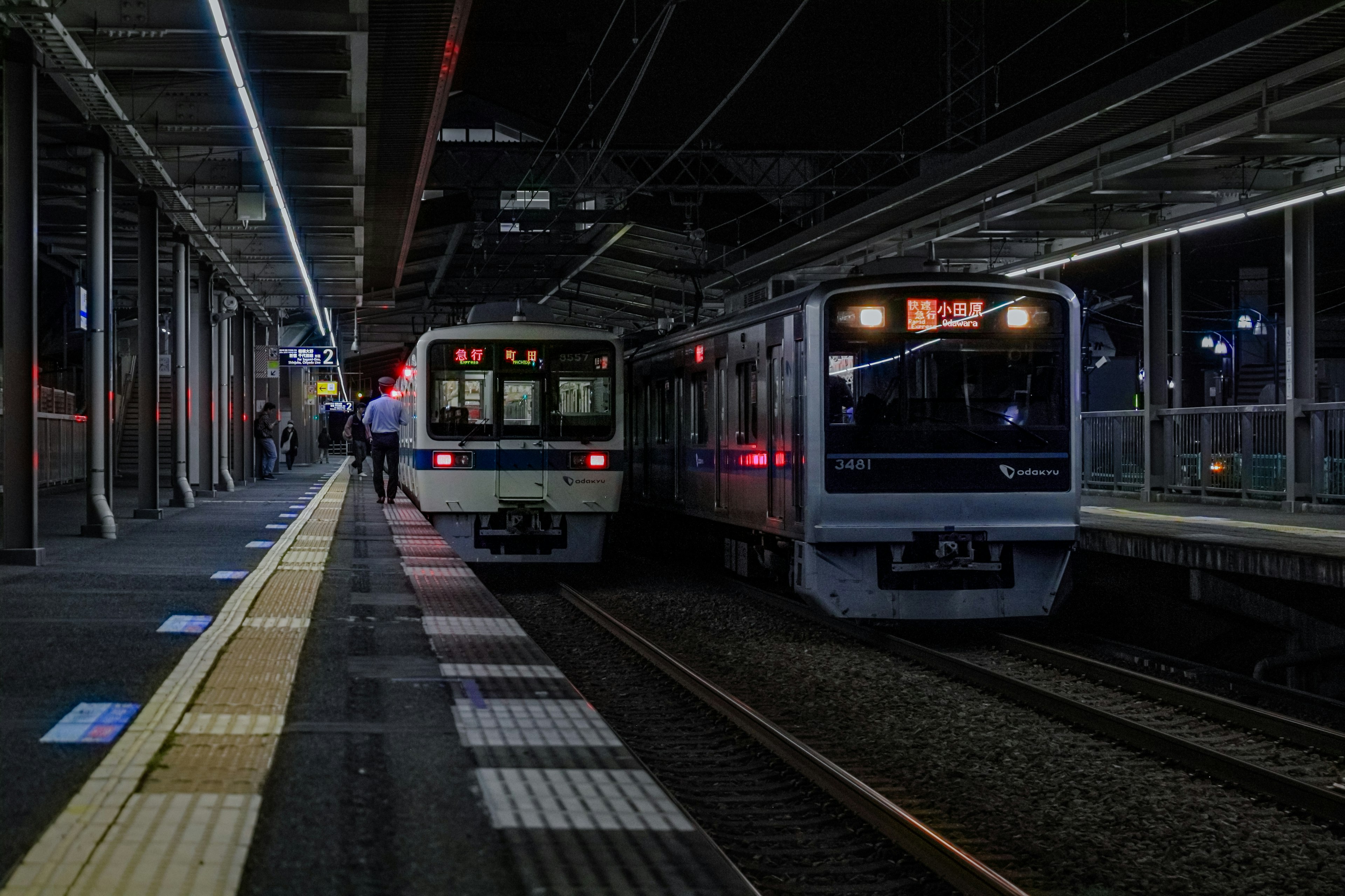 Two trains stopped at a station at night with lighting