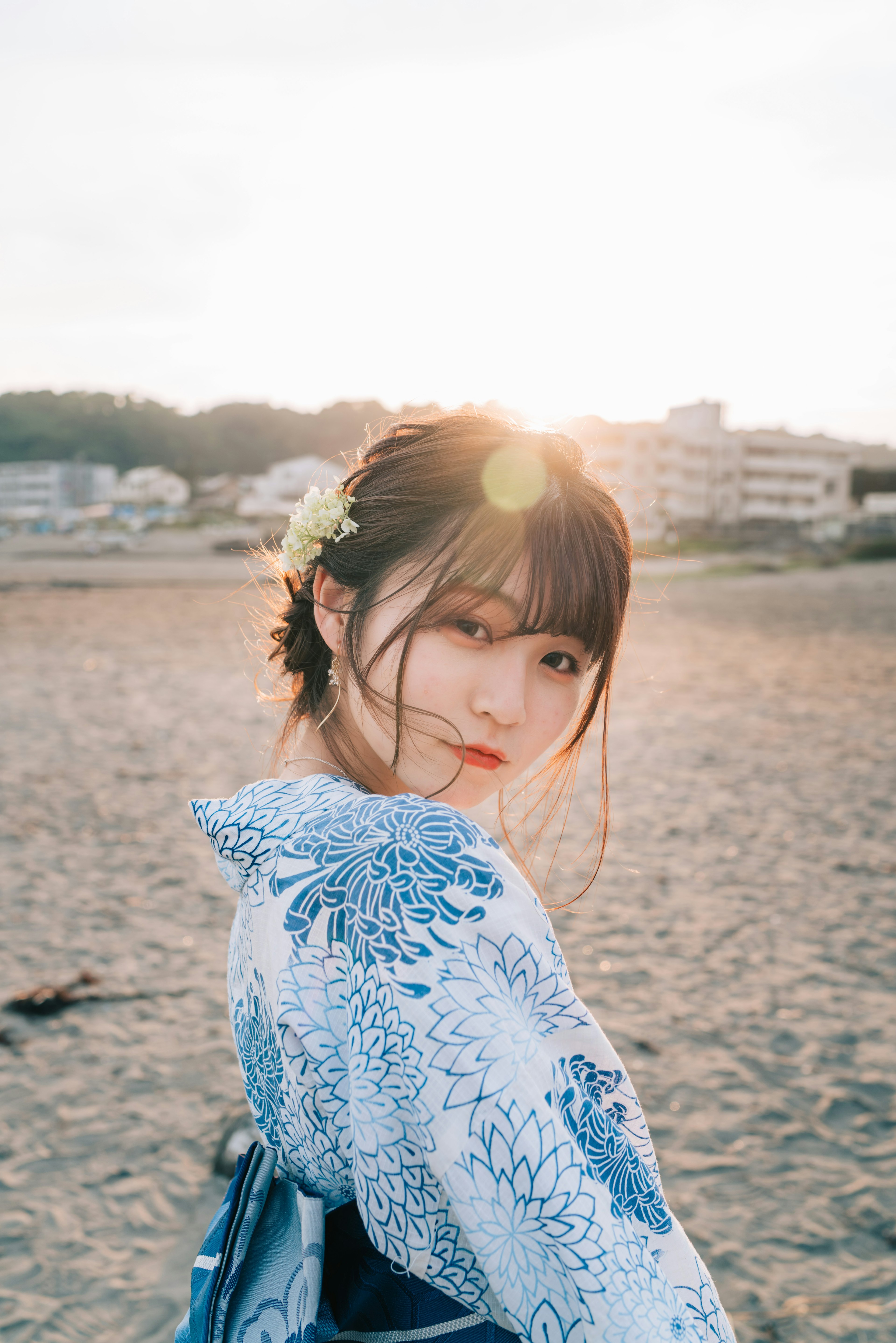 Una donna in kimono blu si gira con il tramonto dietro di lei paesaggio di spiaggia