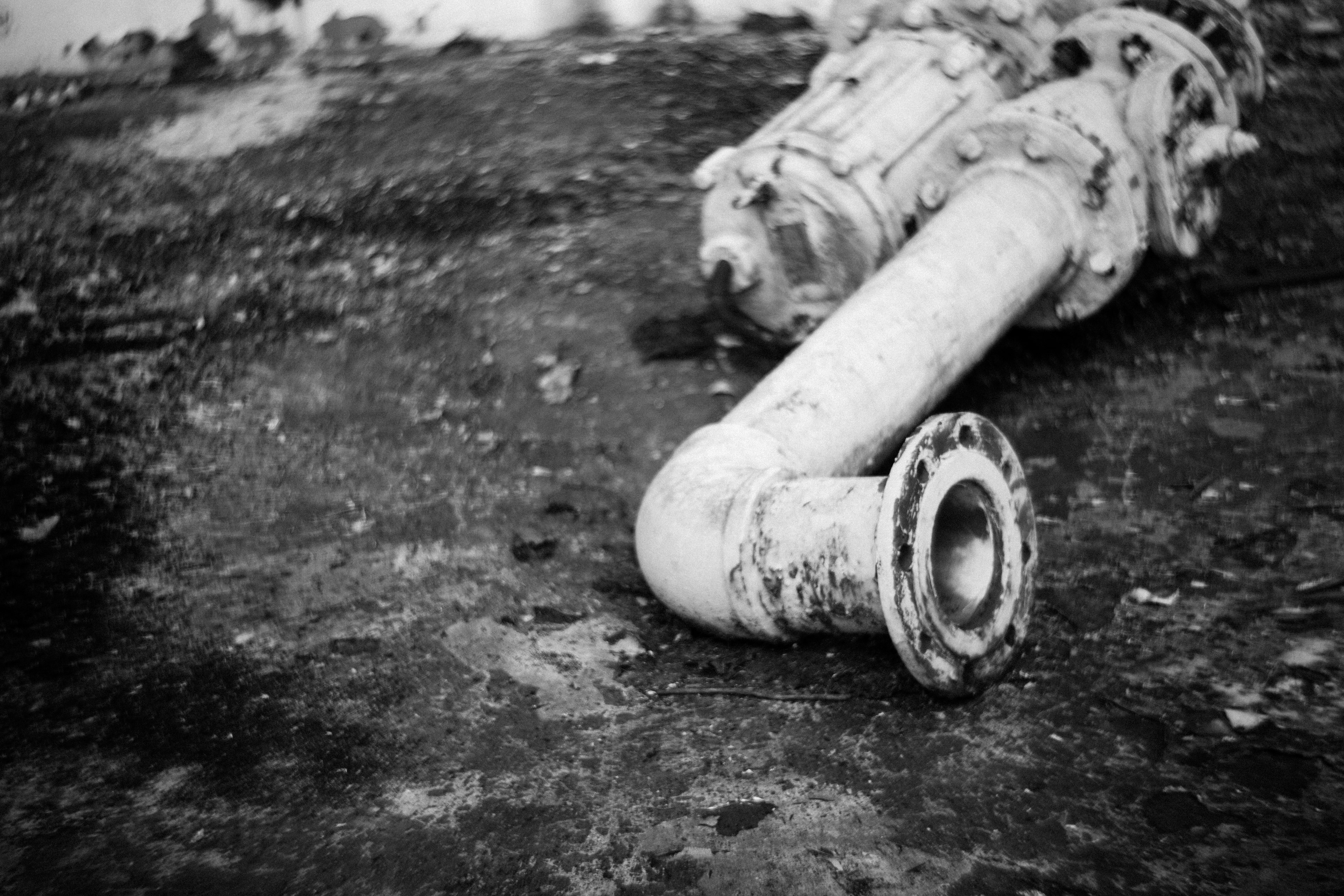 Black and white image of a pipe lying on the ground showing rusty metal parts