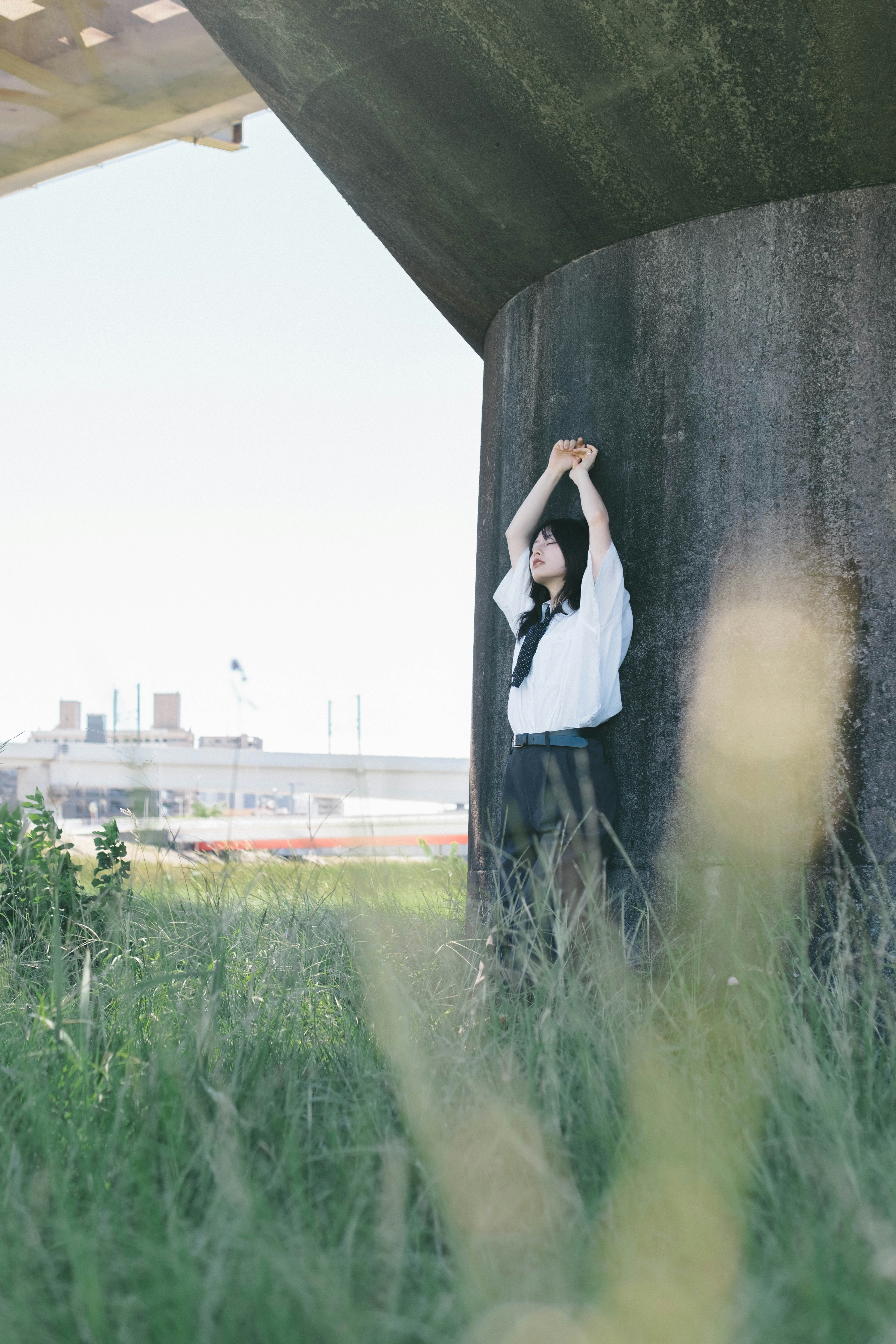 A woman posing beside a concrete pillar surrounded by green grass