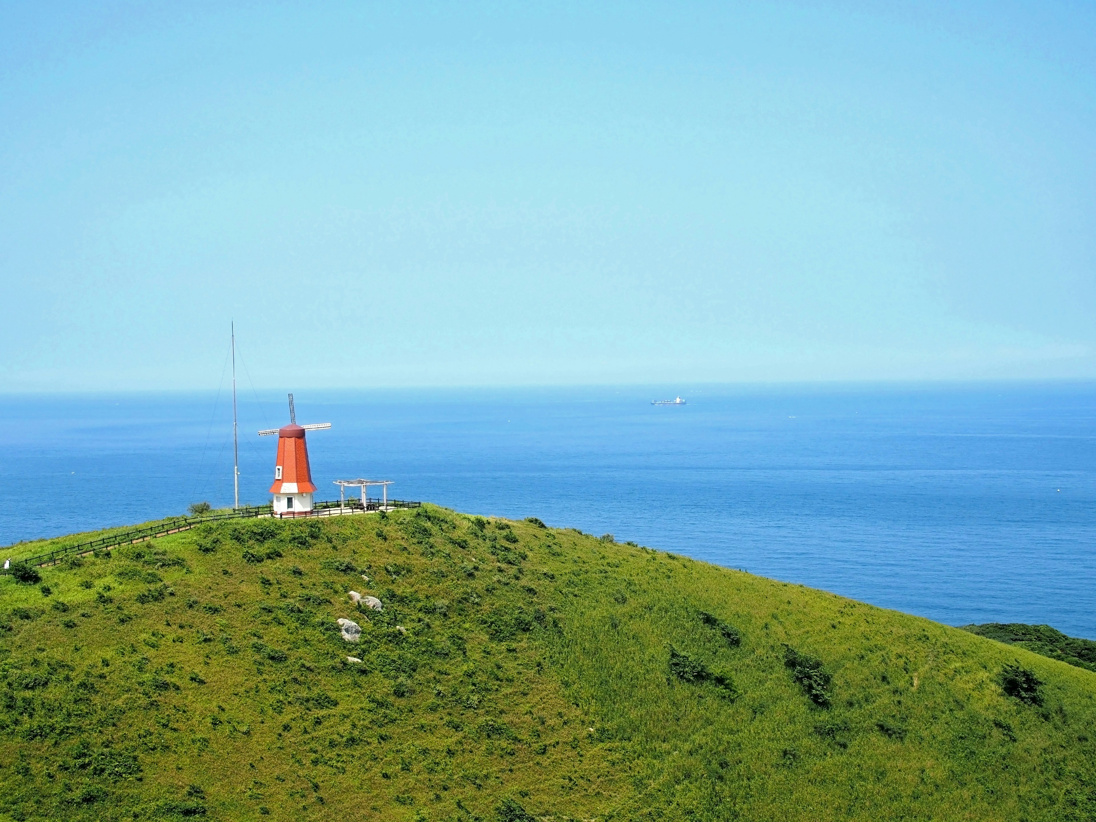 Roter Leuchtturm auf einem grünen Hügel mit Blick auf den blauen Ozean