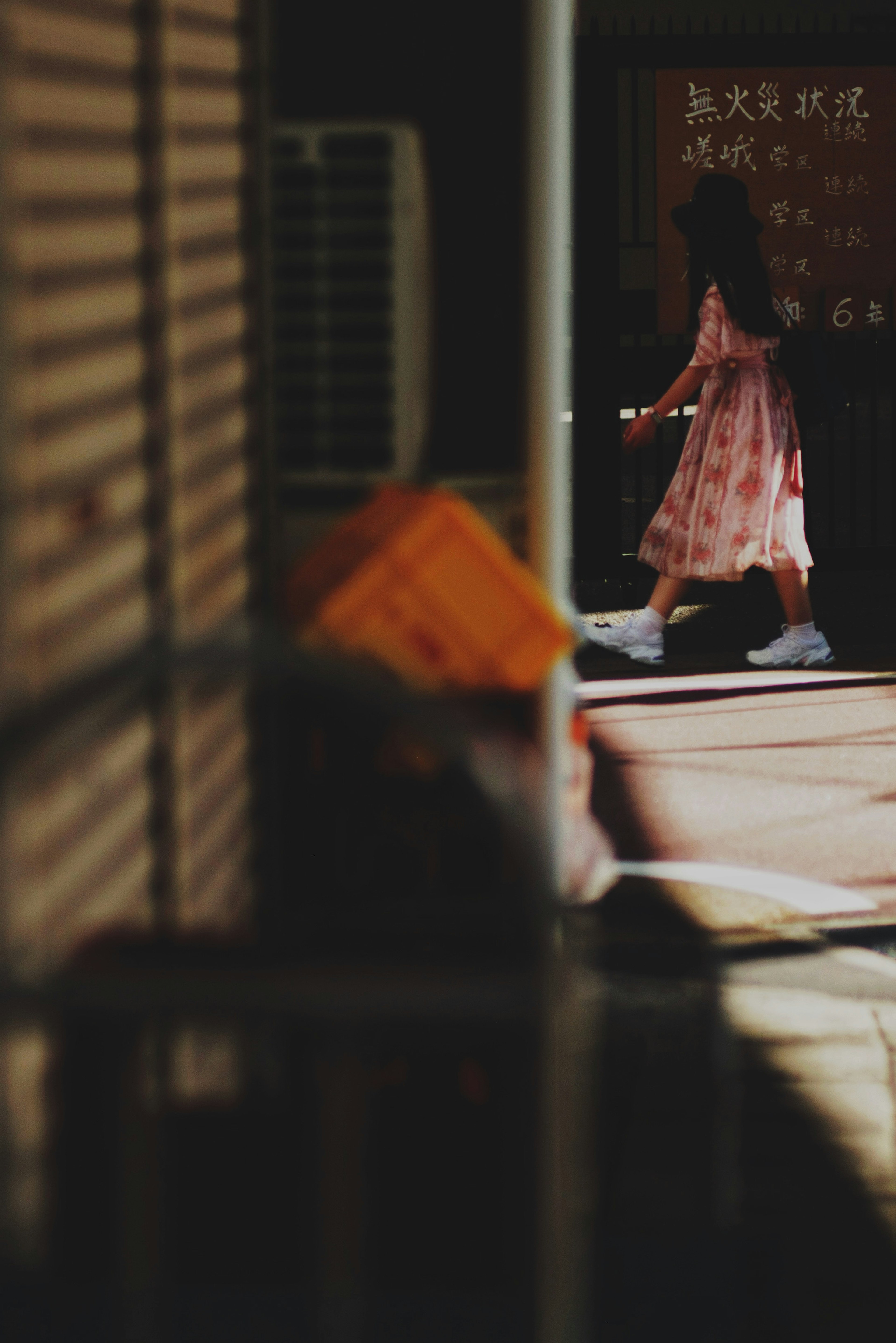 A girl in a light pink dress walking with Chinese characters on a sign in the background