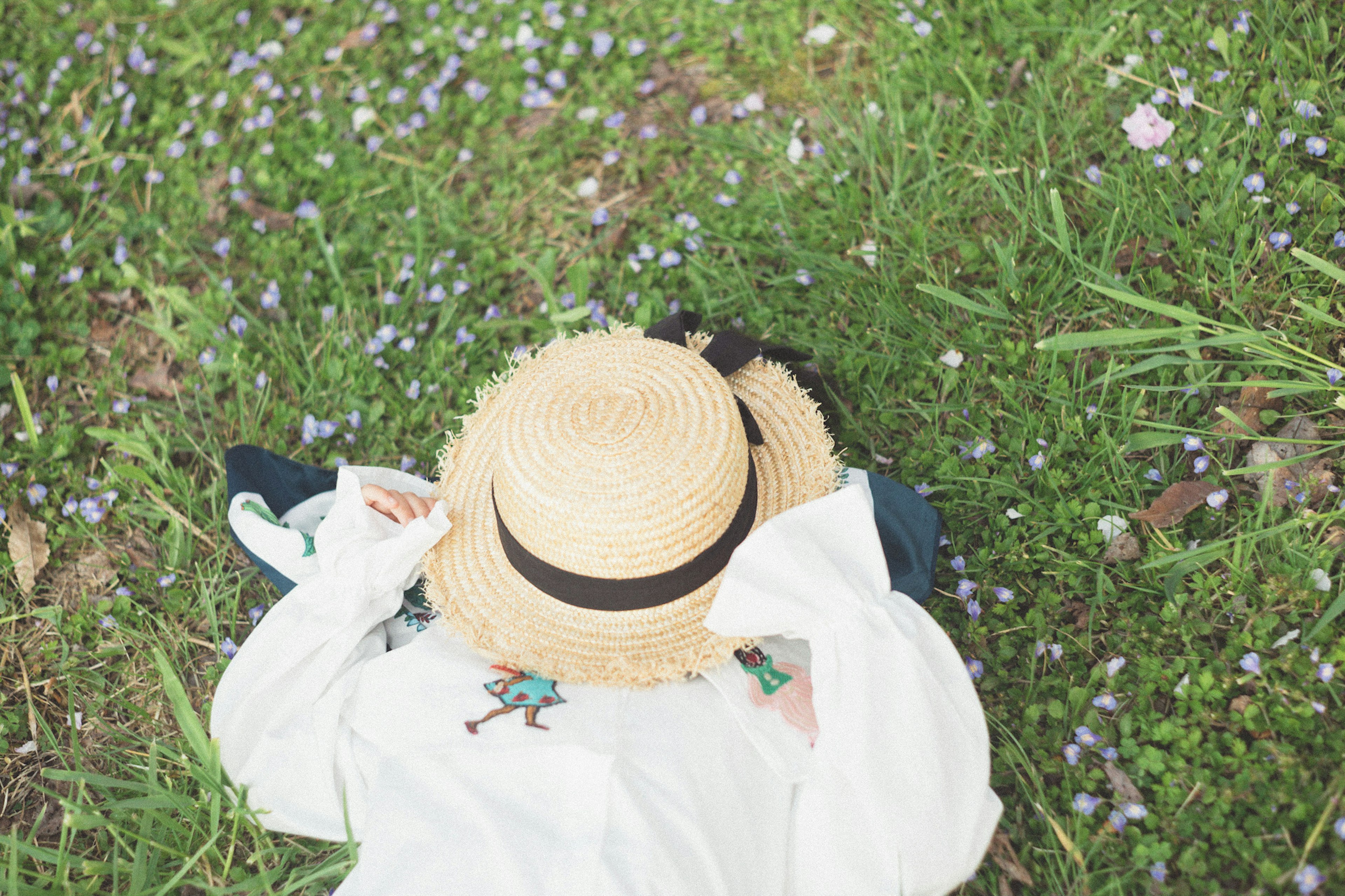 Une femme allongée sur l'herbe portant un chapeau de paille chemise blanche et jupe bleue