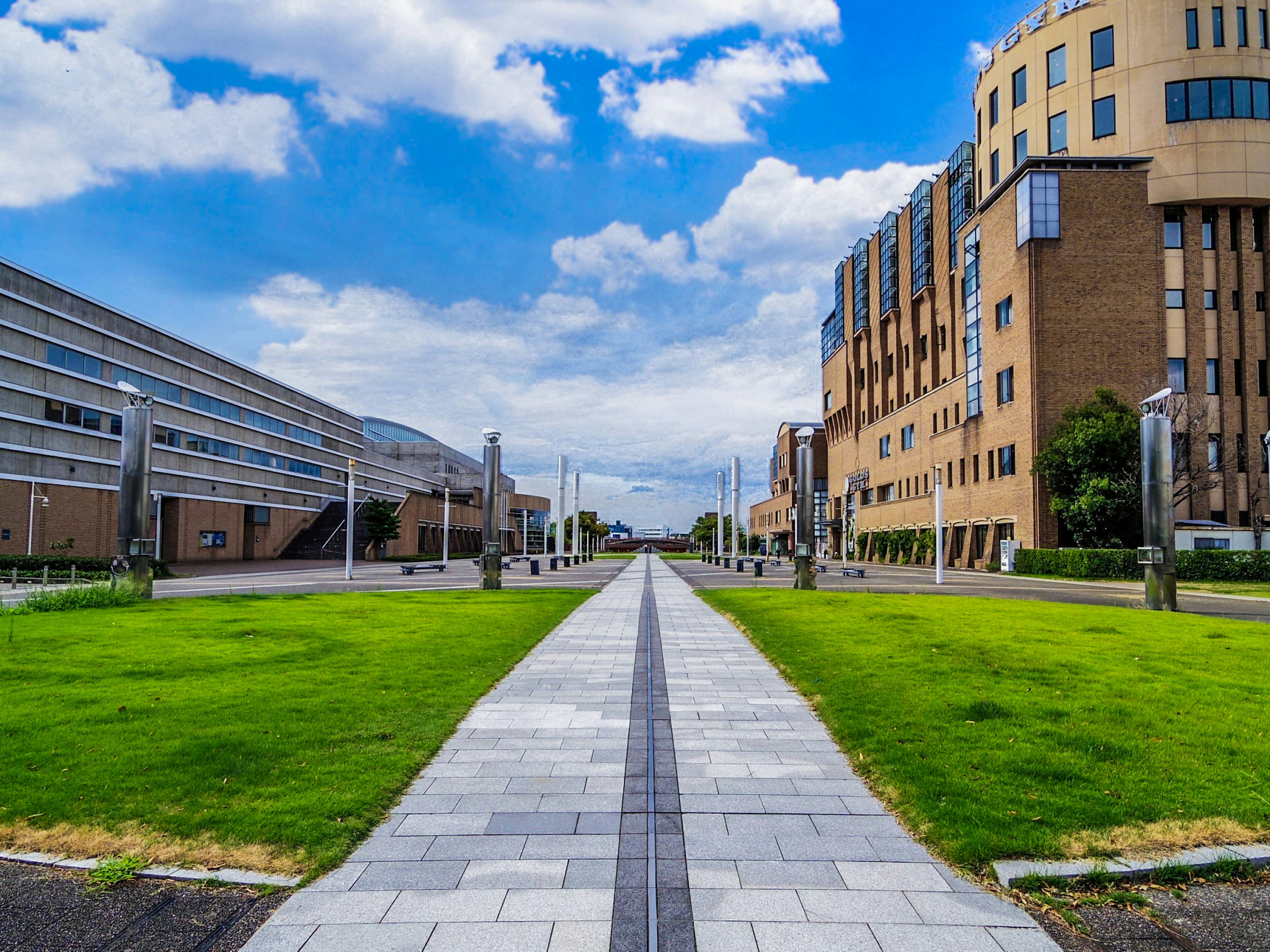 Un paesaggio con erba verde e un sentiero di pietra sotto un cielo blu Edifici moderni a sinistra e un edificio di design diverso a destra