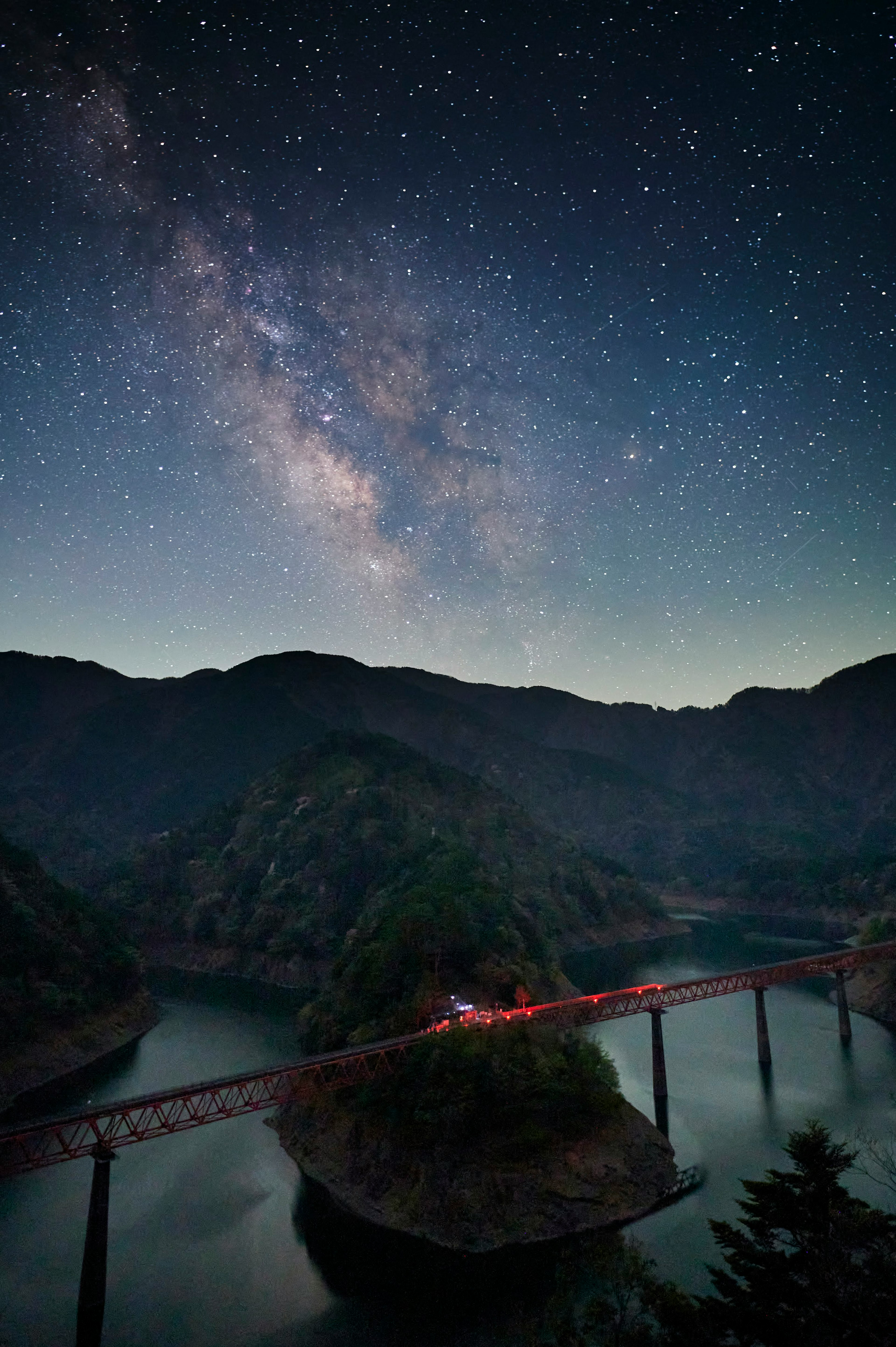 美しい星空の下に広がる山々と湖の風景に架かる橋