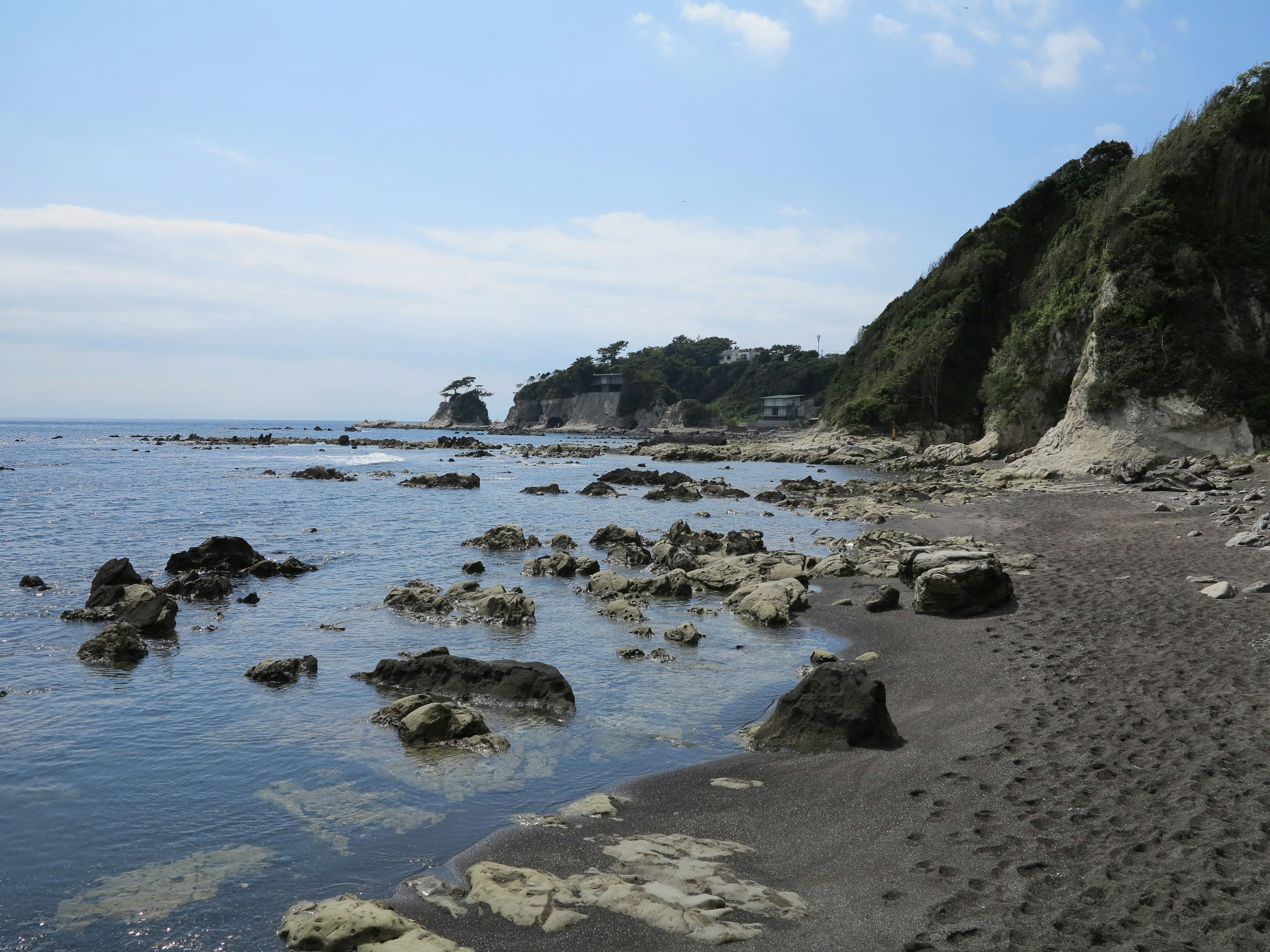 Pemandangan pantai dengan batu dan pasir di bawah langit biru dan laut tenang