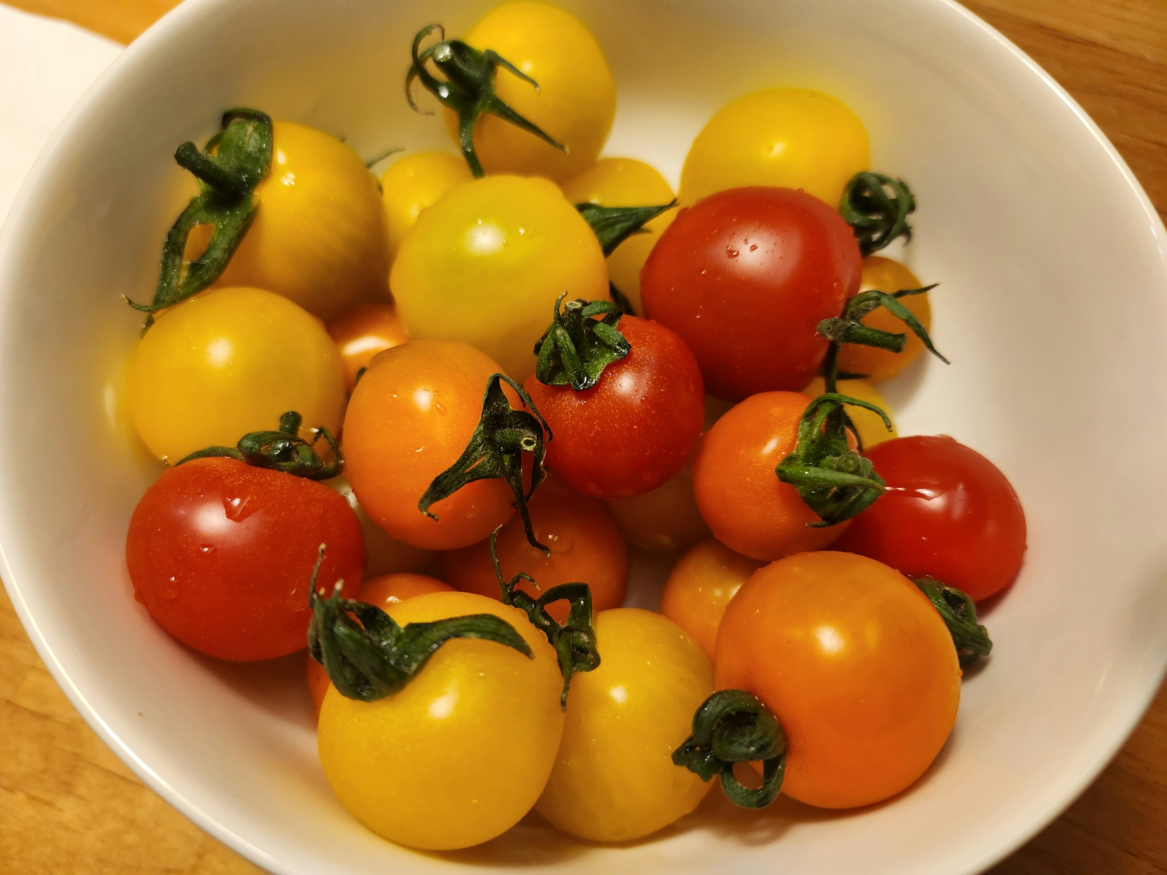 Un tazón blanco lleno de tomates cherry de varios colores