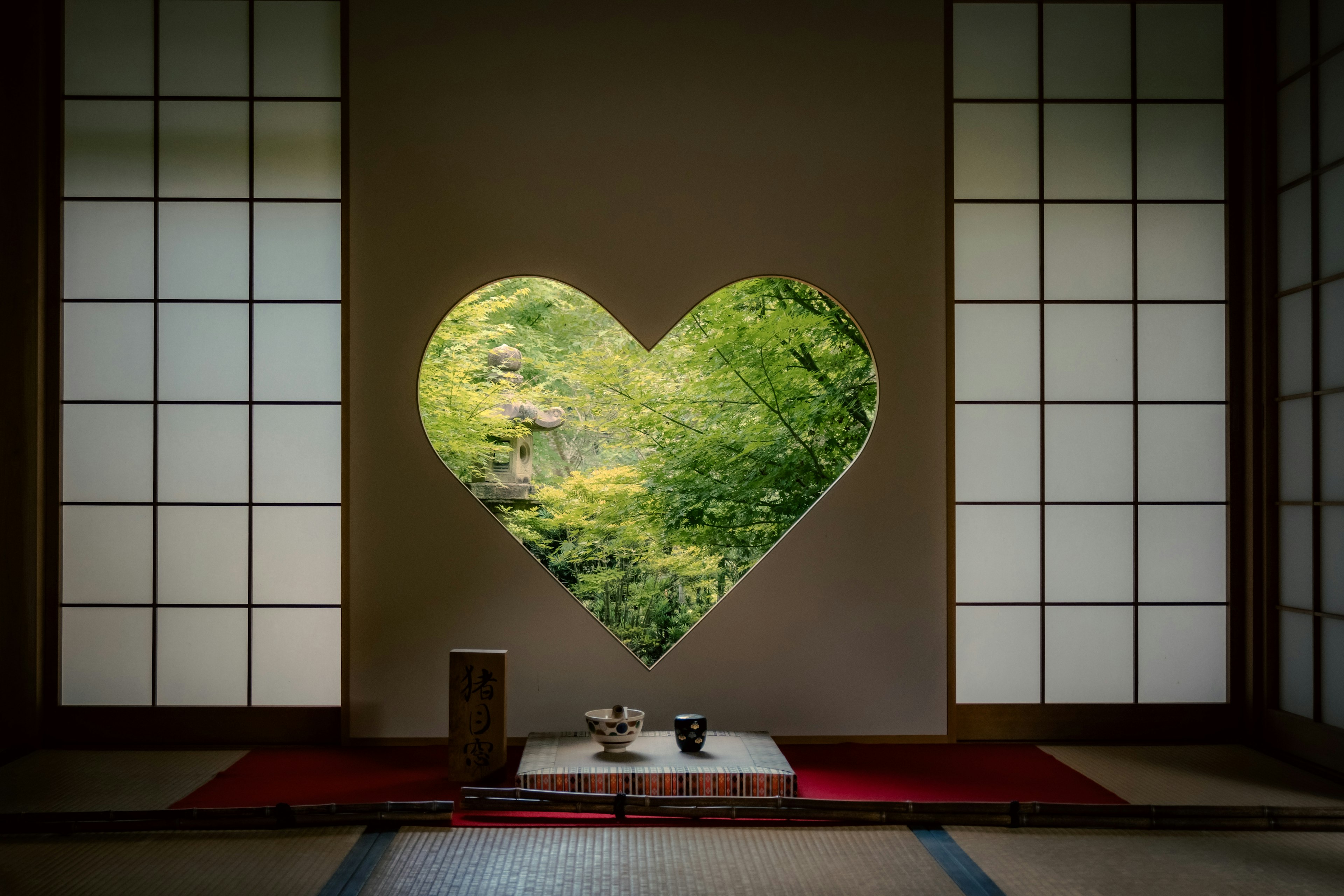 Ventana en forma de corazón que revela un paisaje verde y un interior japonés tradicional