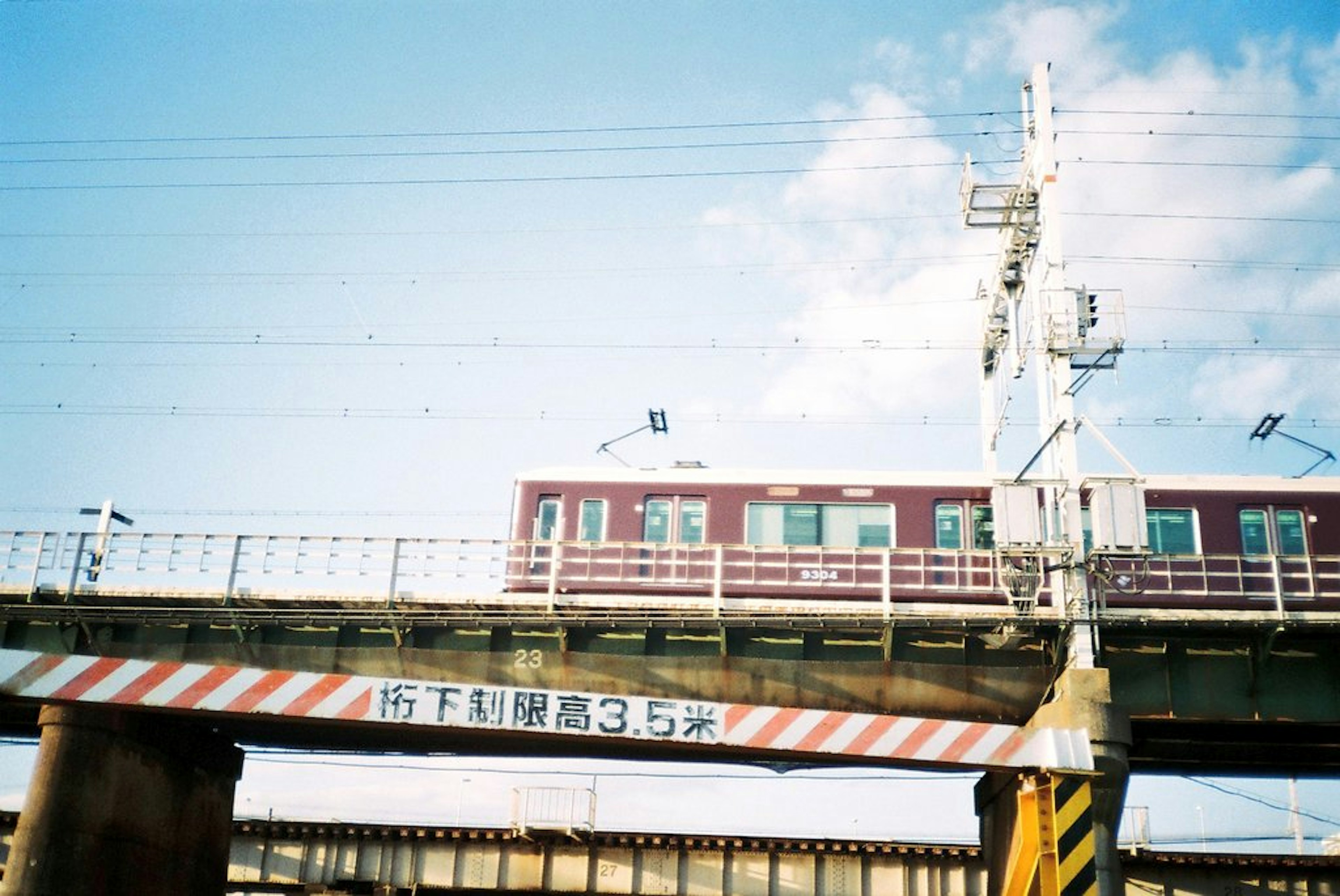 Un train rouge sur un pont élevé sous un ciel bleu avec un signal à proximité