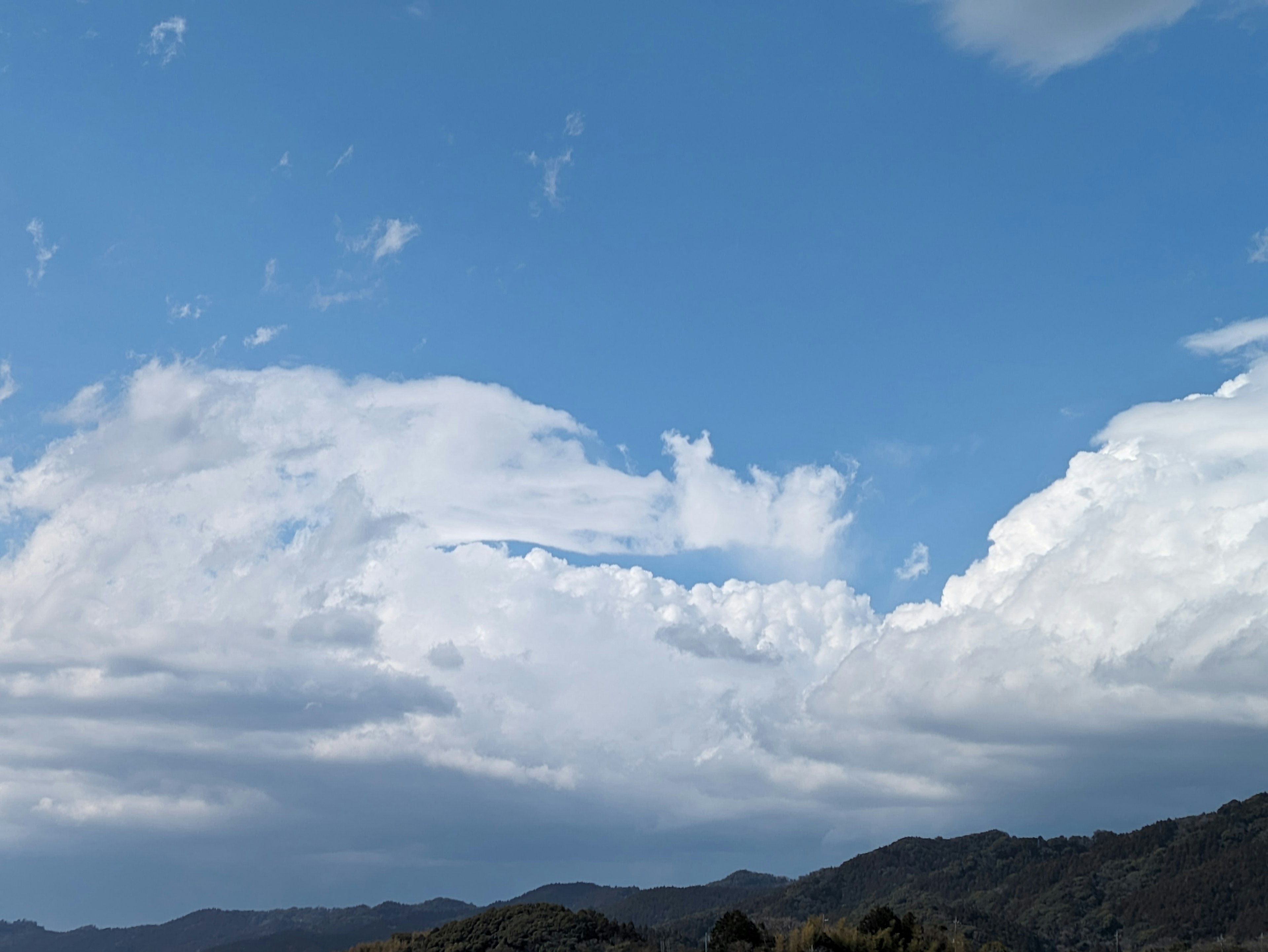 A landscape featuring a blue sky with white clouds and mountains in the background