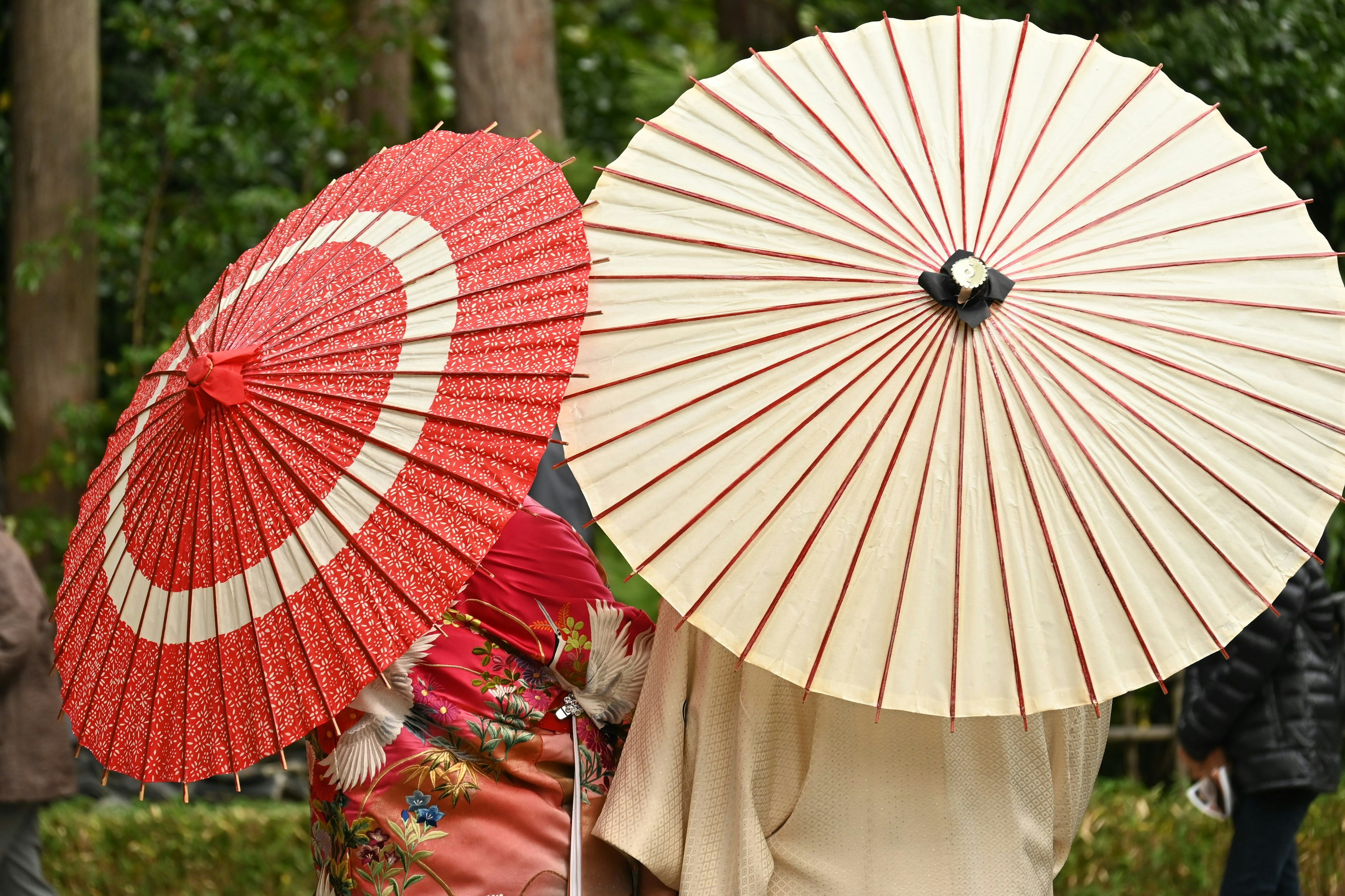 Two figures holding traditional umbrellas Red and white parasols with intricate designs