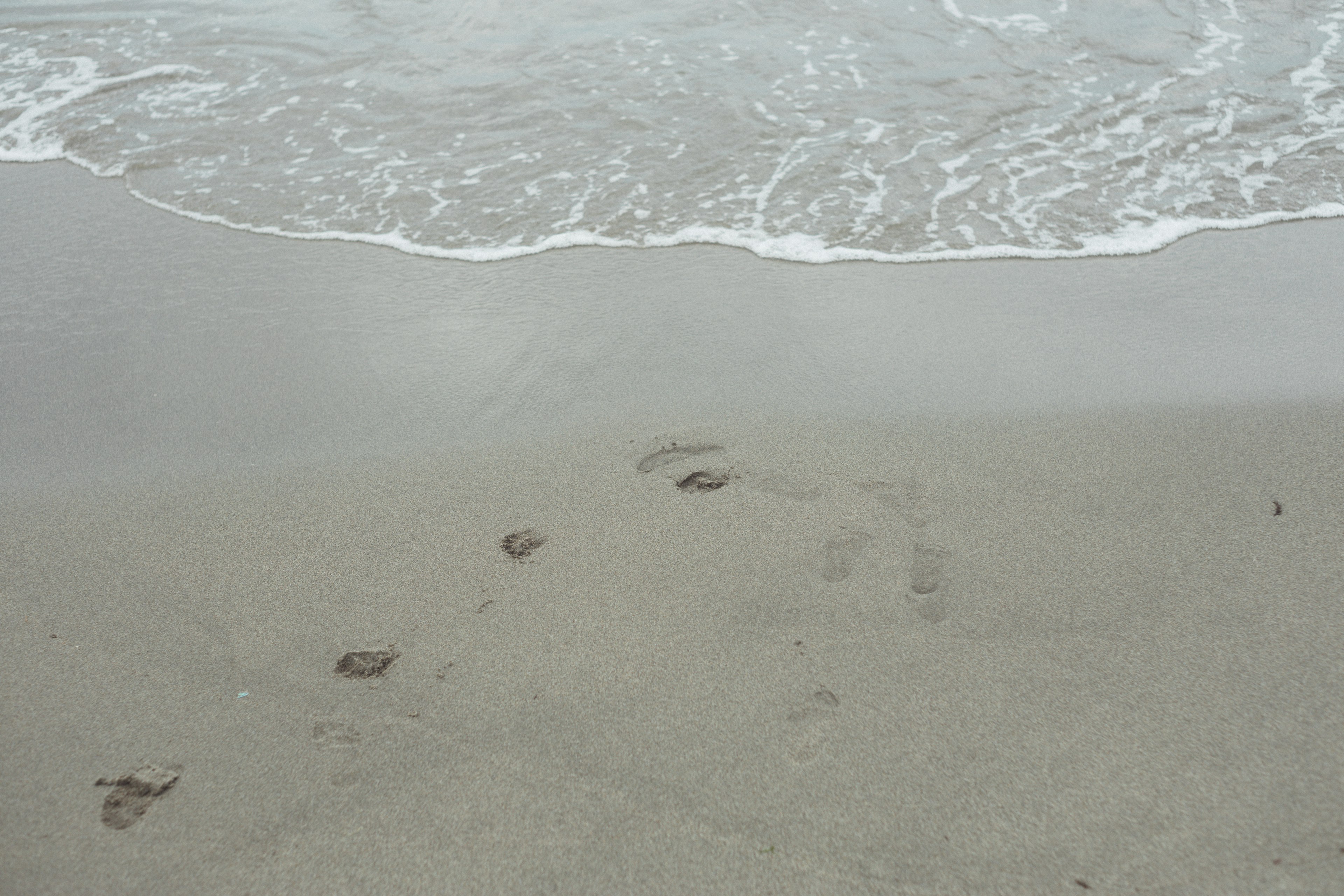 Footprints on a sandy beach with waves approaching