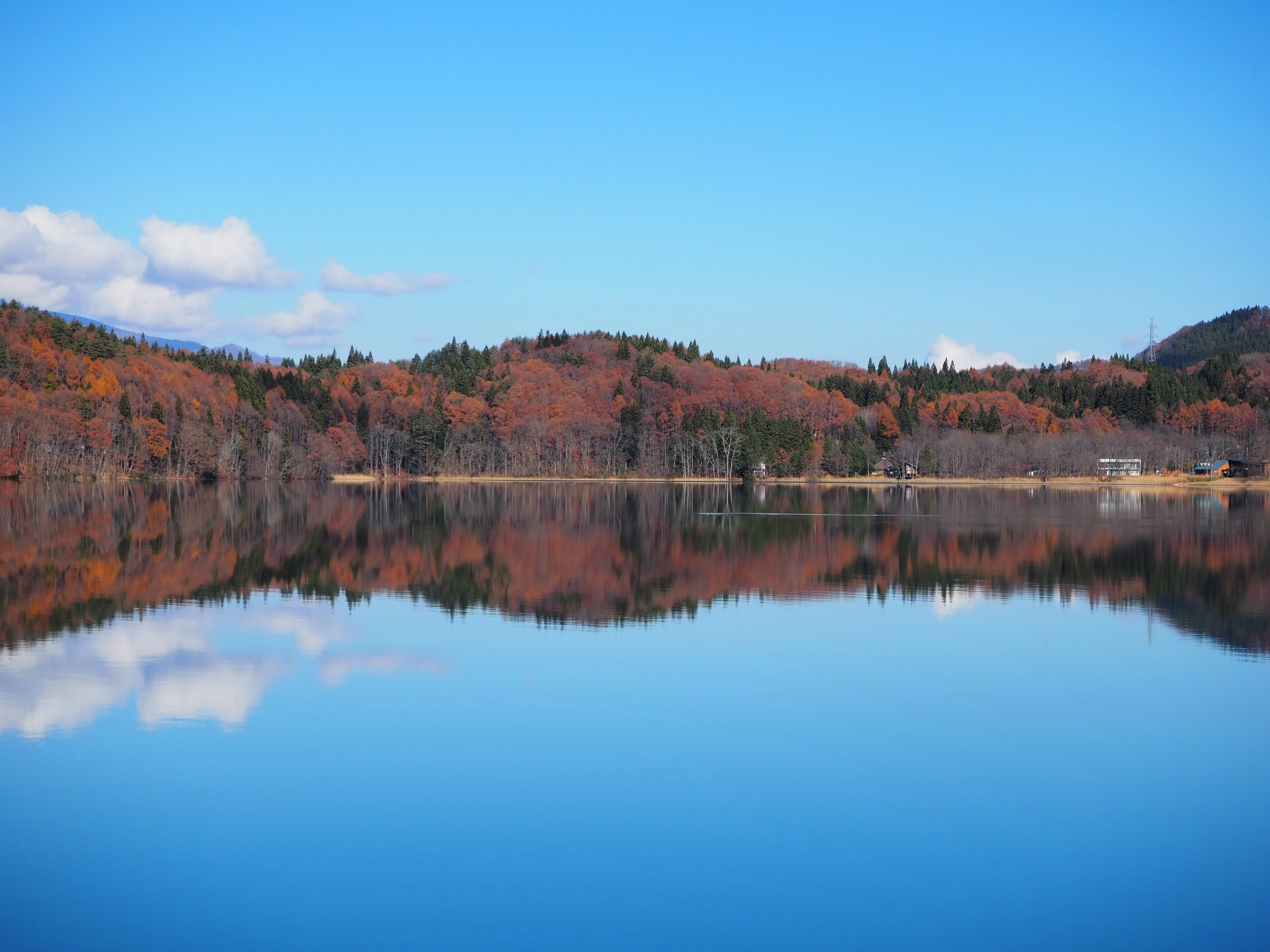 Ruhige Seenlandschaft mit blauem Himmel und herbstlichen Laub im ruhigen Wasser reflektiert