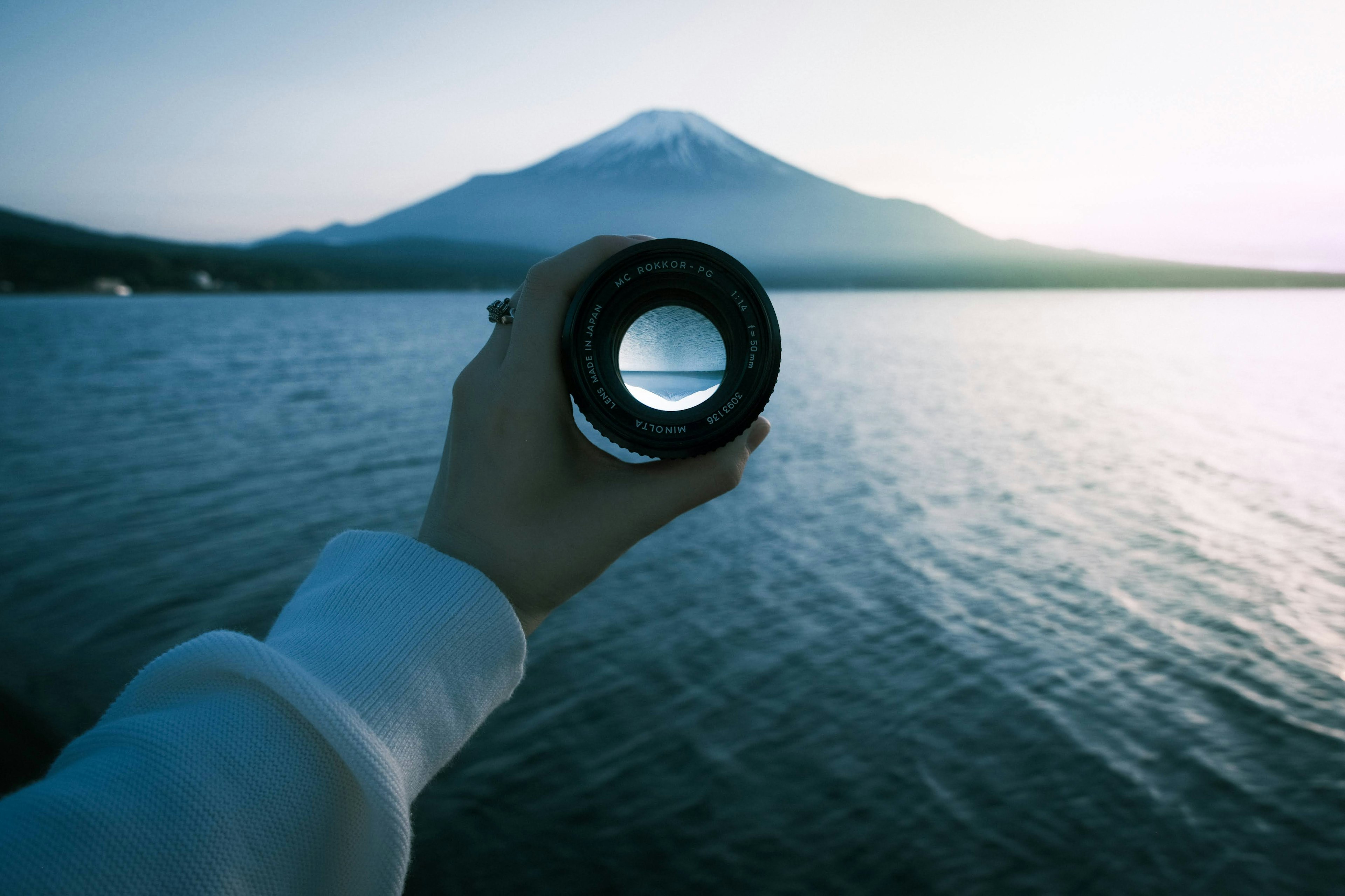 Una mano che tiene un obiettivo inquadrando il monte Fuji con un lago sereno