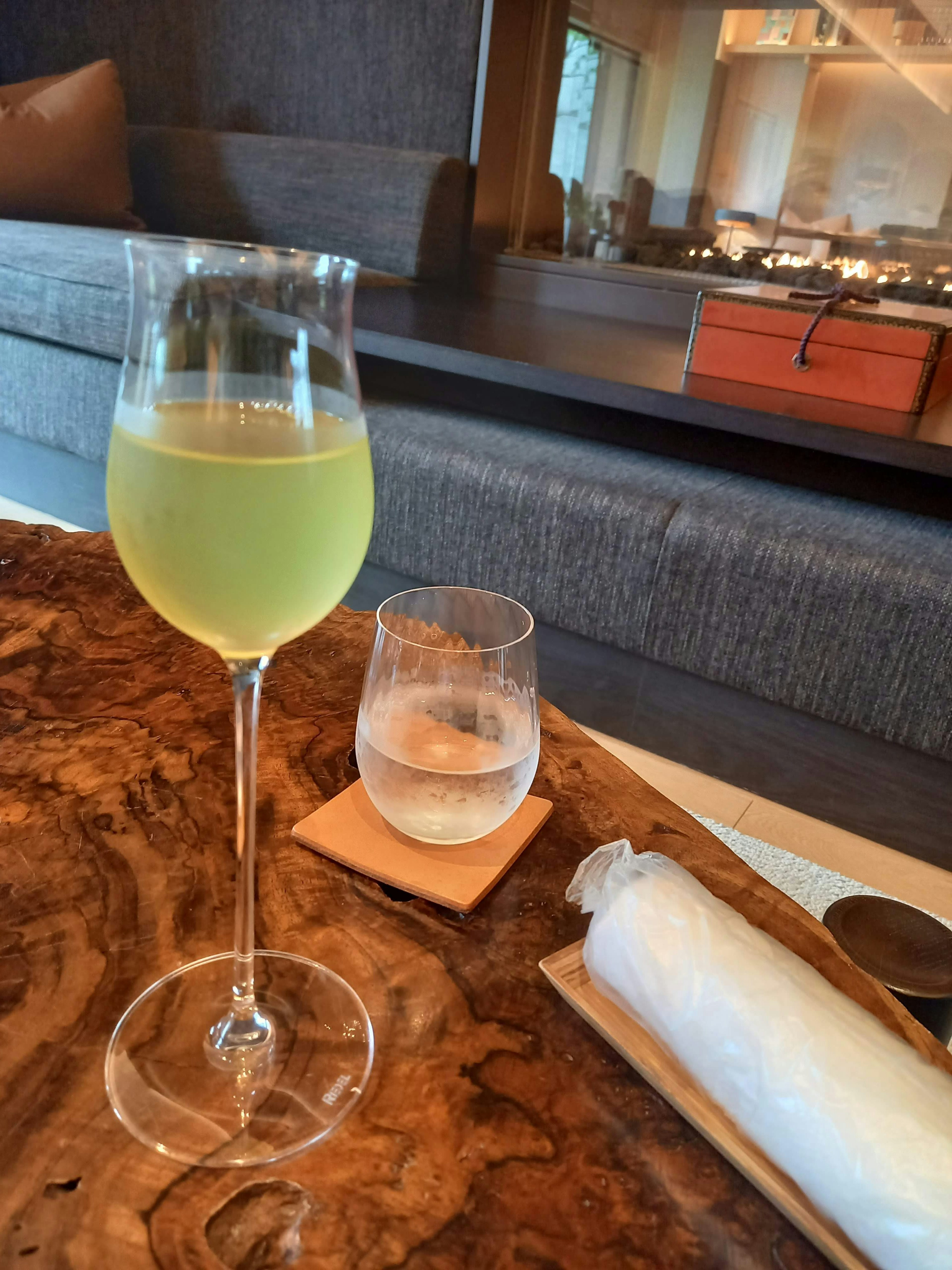 A tall glass with green drink and a short glass with water on a wooden table