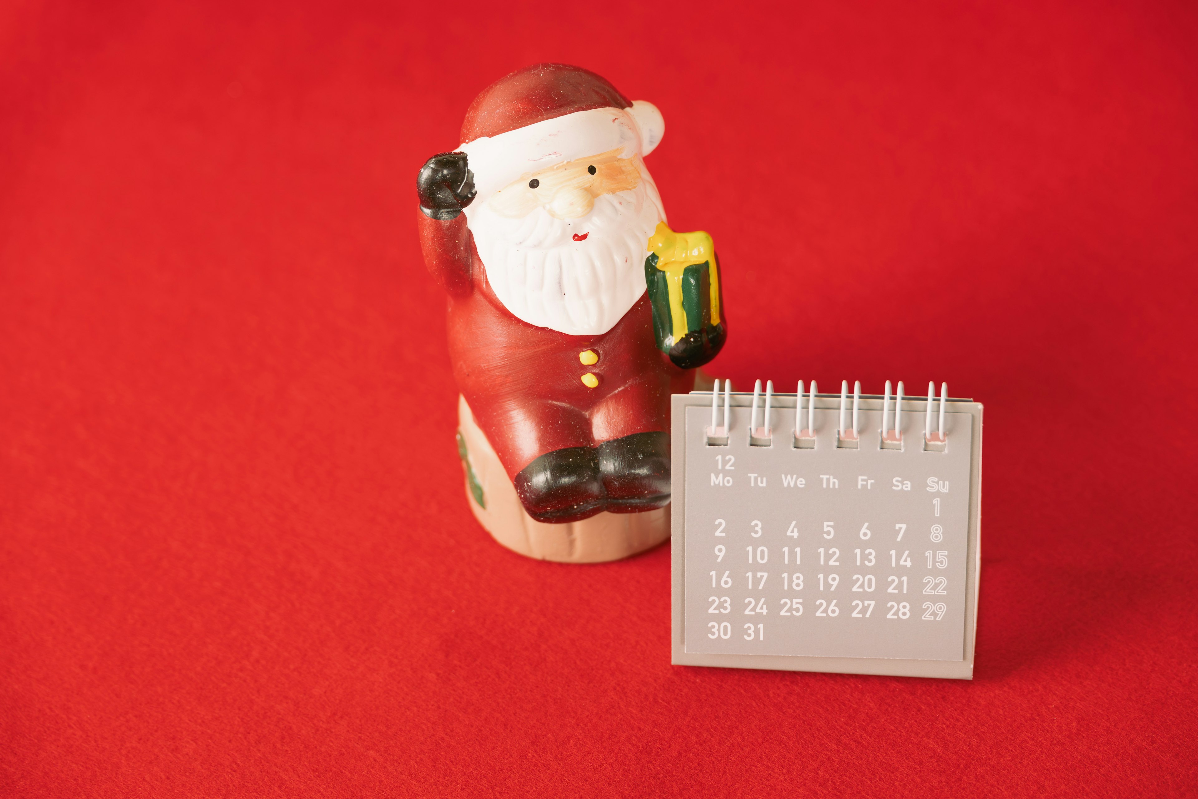 Santa Claus figurine next to a calendar on a red background