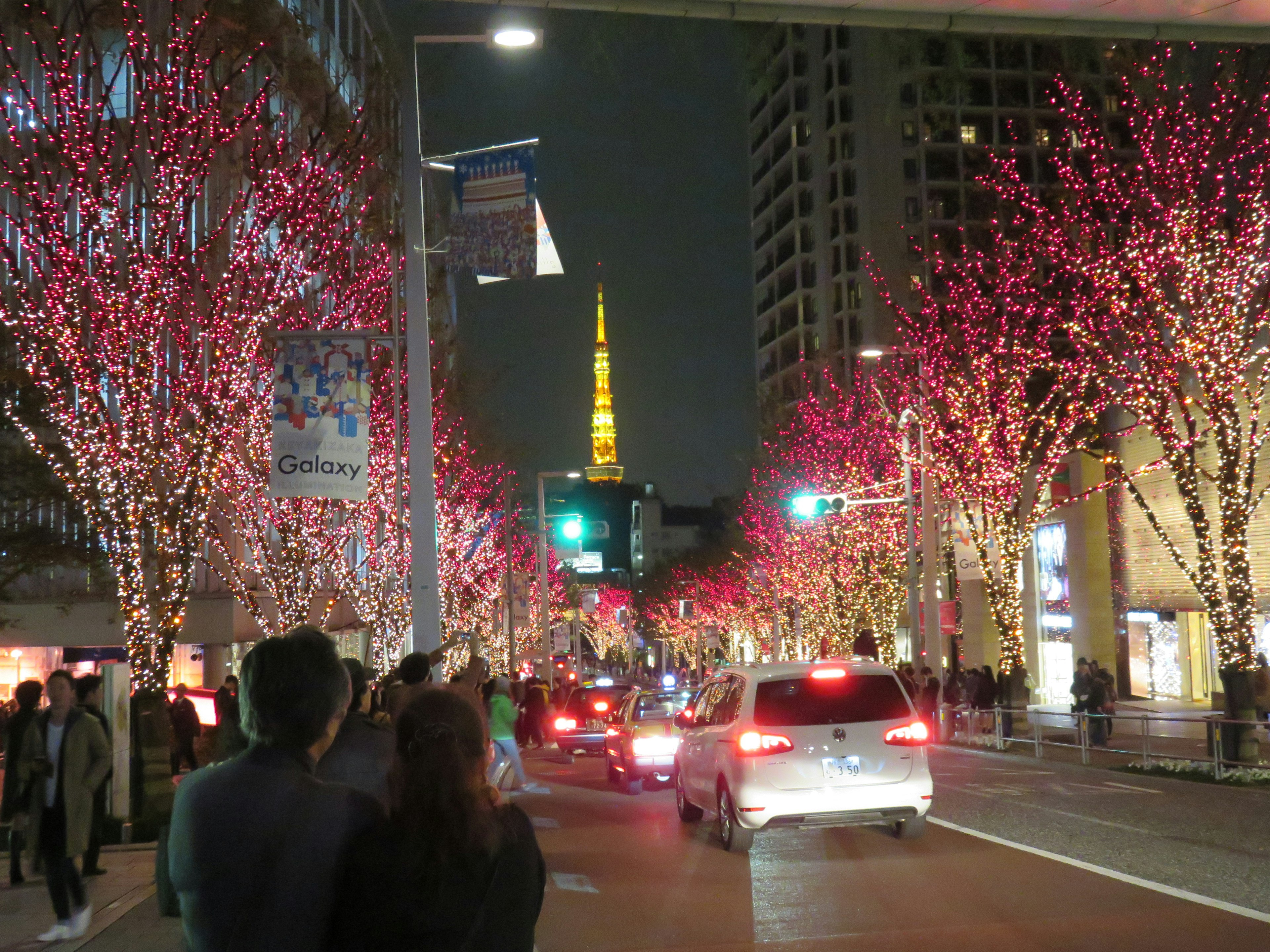 Stadtstraße bei Nacht mit pink beleuchtetem Bäumen und dem Tokyo Tower im Hintergrund