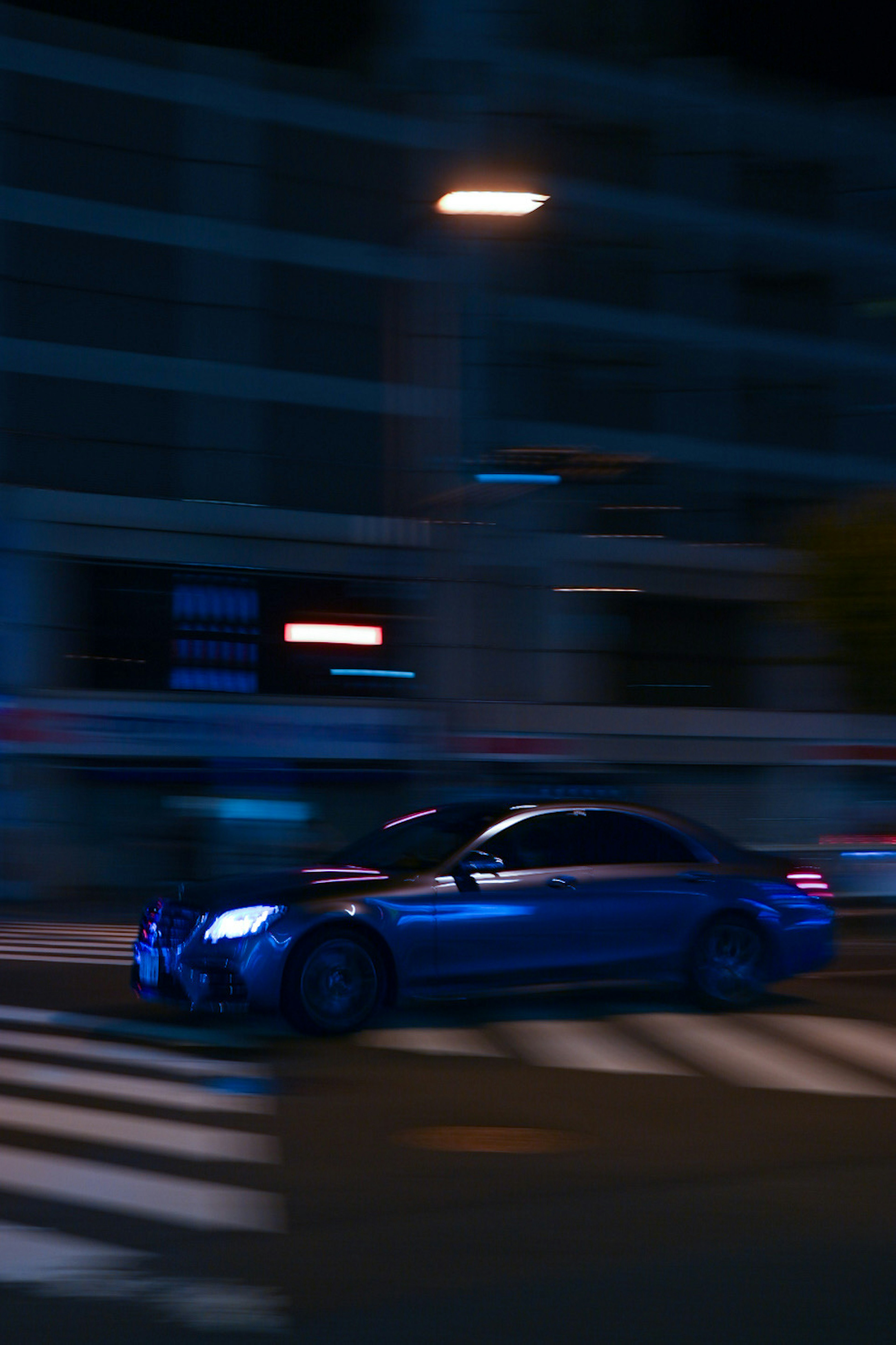 A blue car speeding through a city street at night