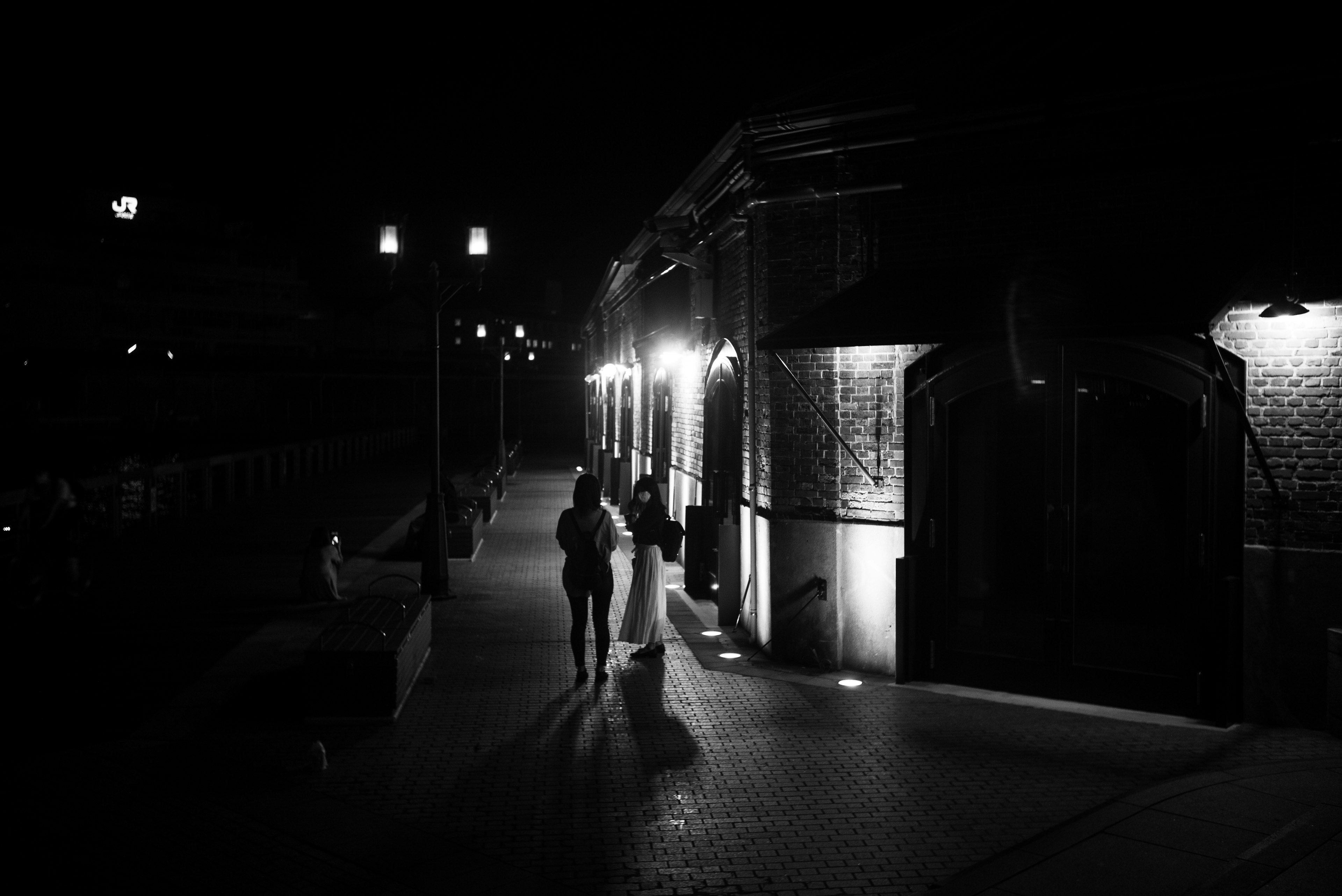 Siluetas de dos personas caminando por una calle tranquila de noche con luces llamativas