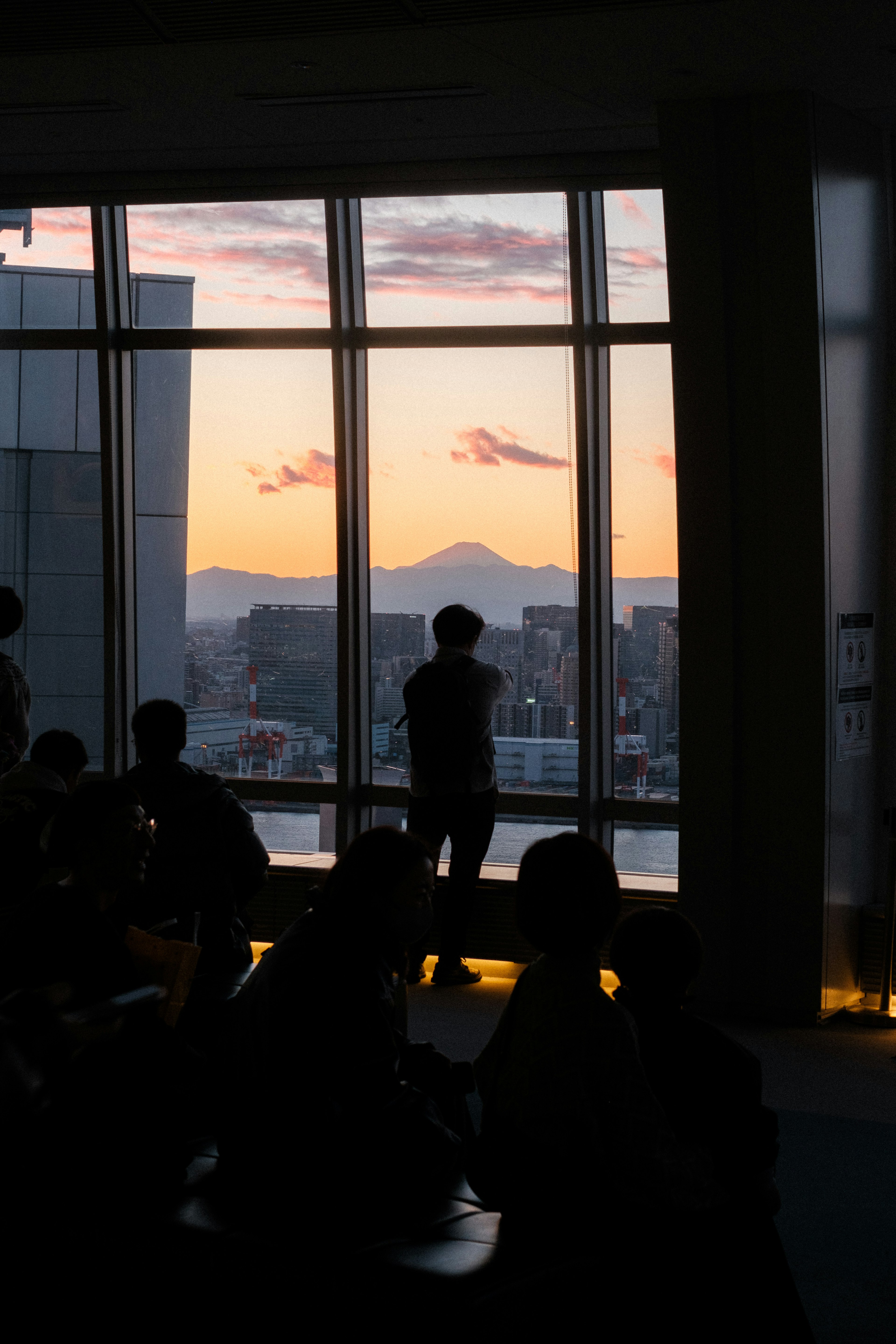 Silhouette of a person standing by a window with a sunset and cityscape in the background