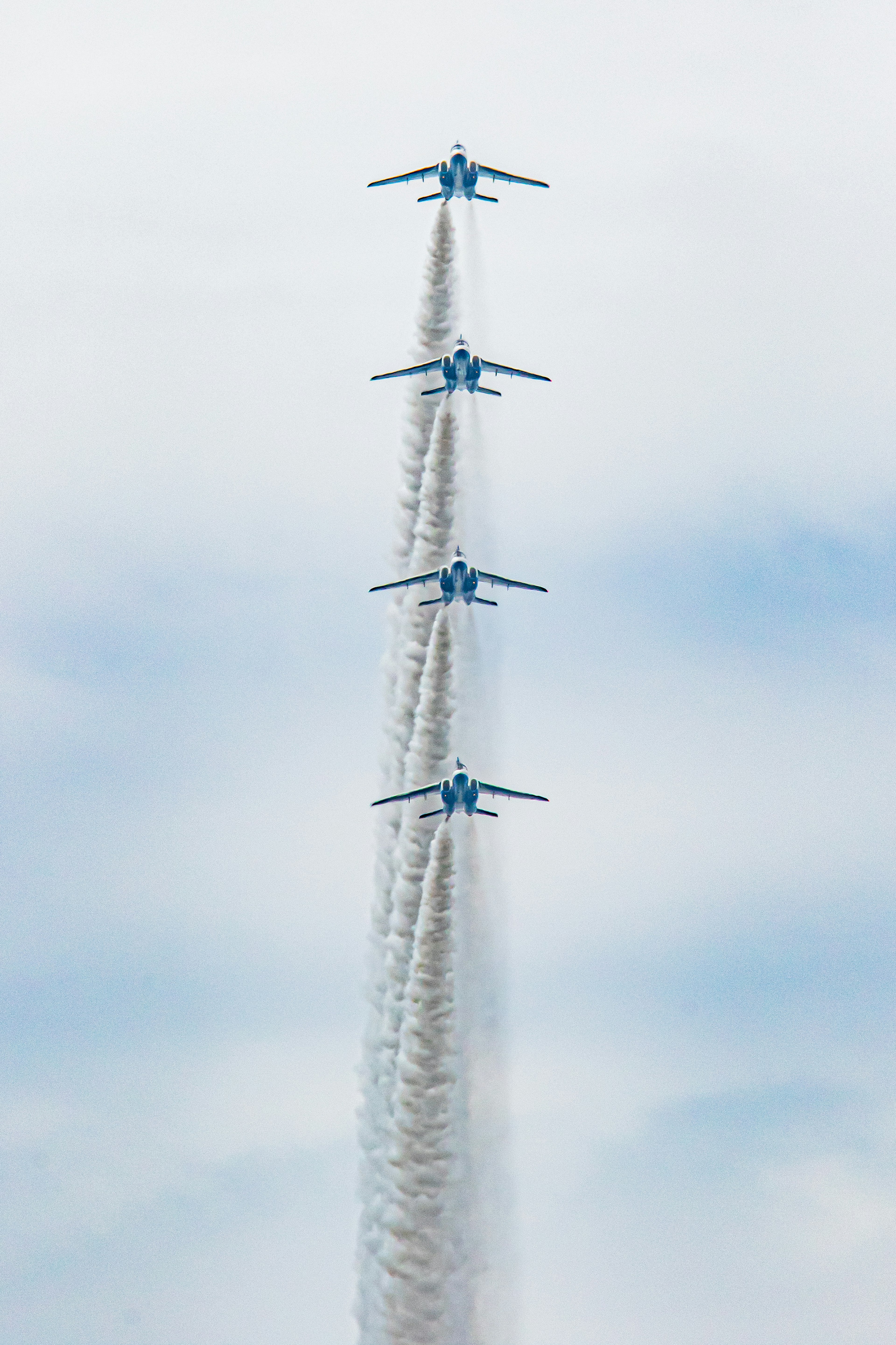 Cuatro aviones azules volando en formación vertical con estelas de humo