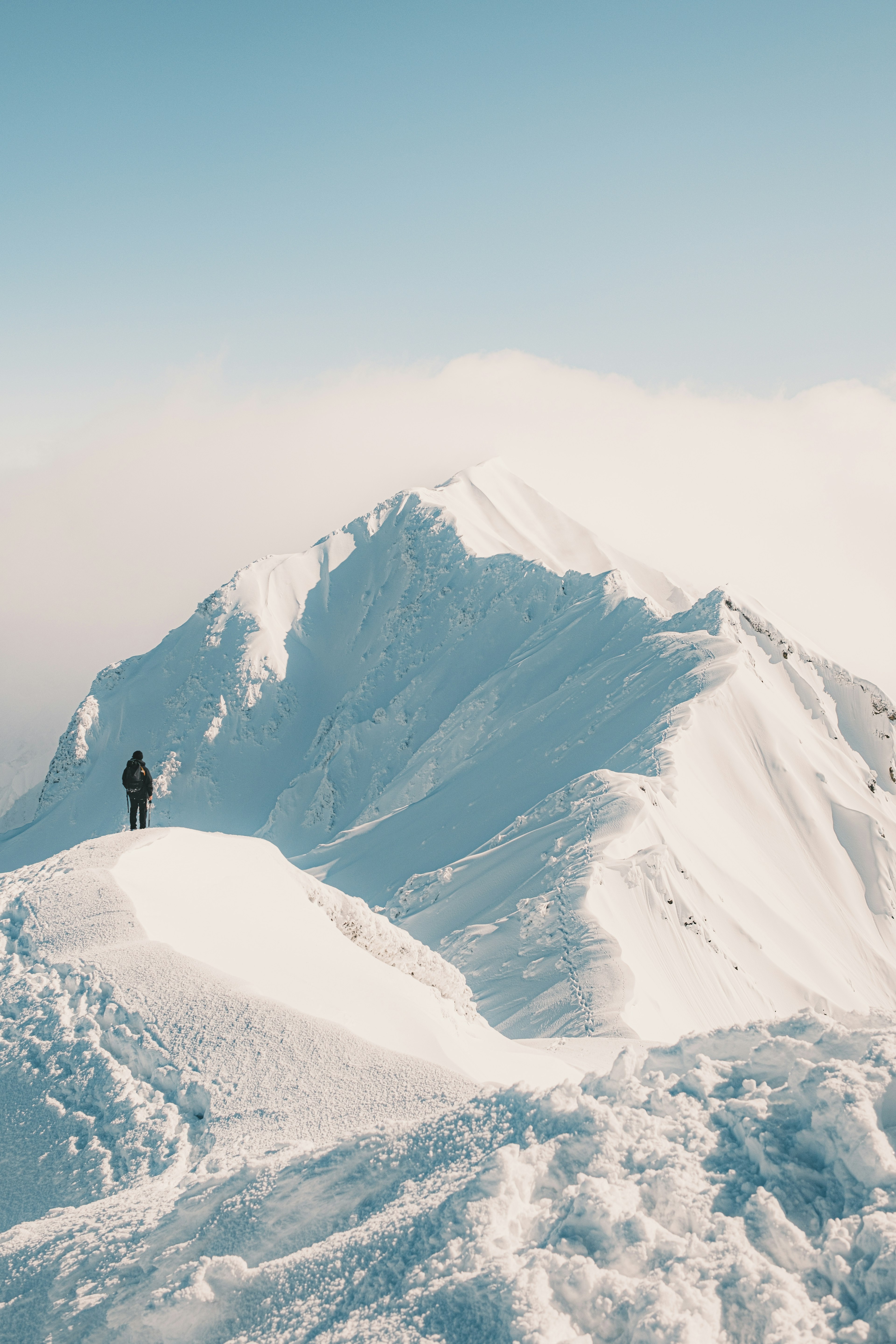 Silhouette of a climber standing on a snow-covered mountain peak