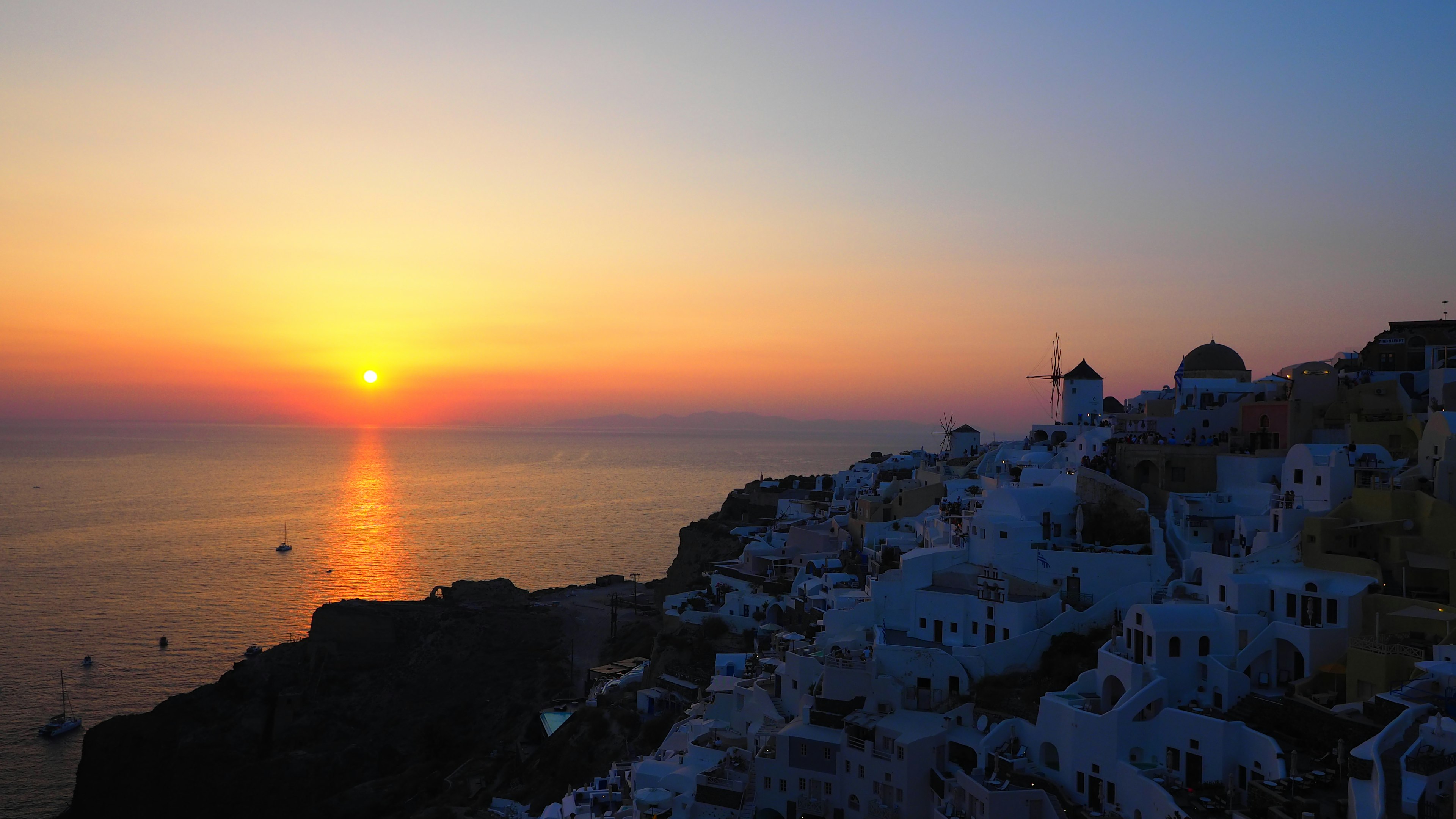 Beeindruckender Sonnenuntergang über Santorin mit weißen Gebäuden und ruhigem Meer