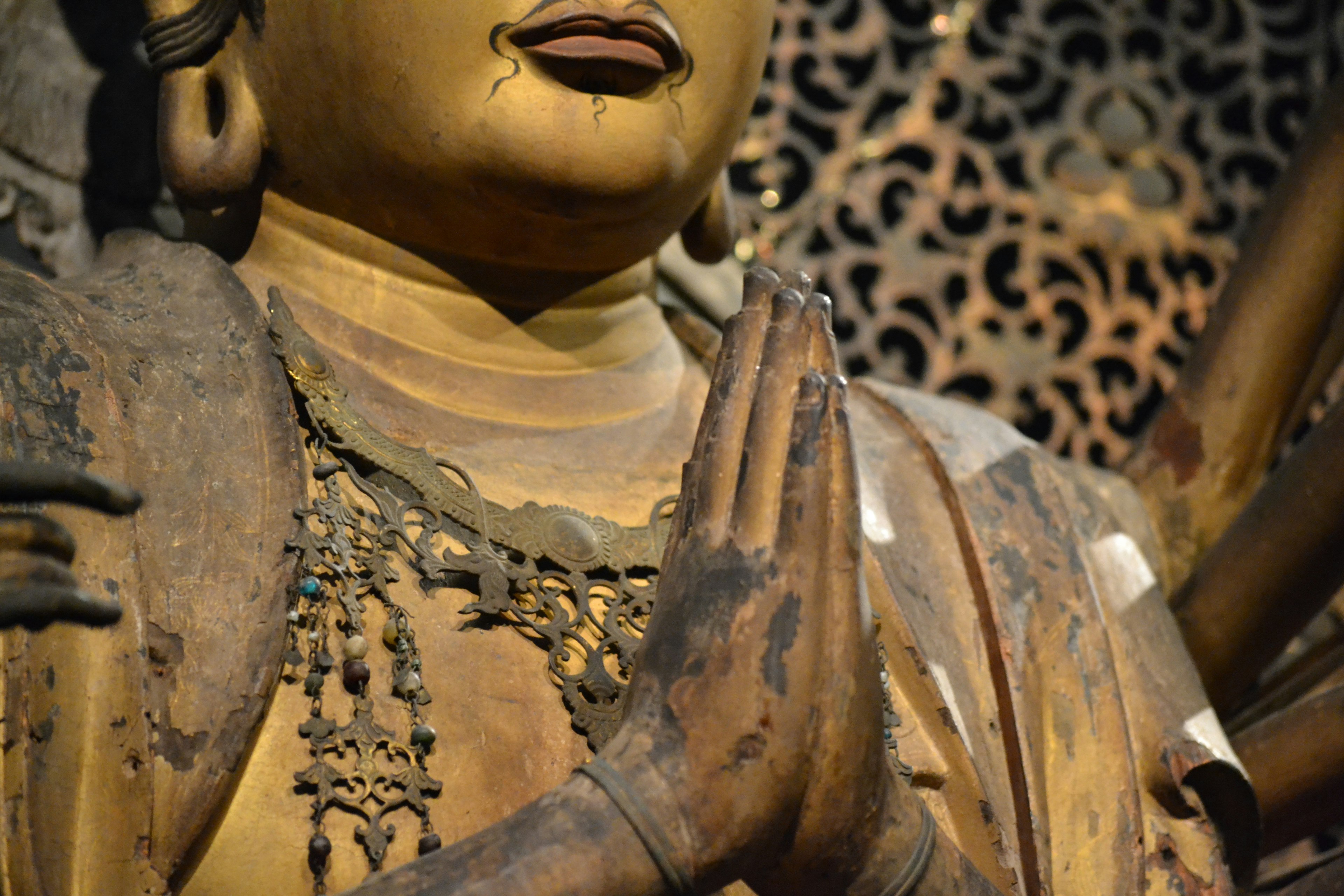 Close-up of a golden Buddha statue with hands in prayer and intricate background