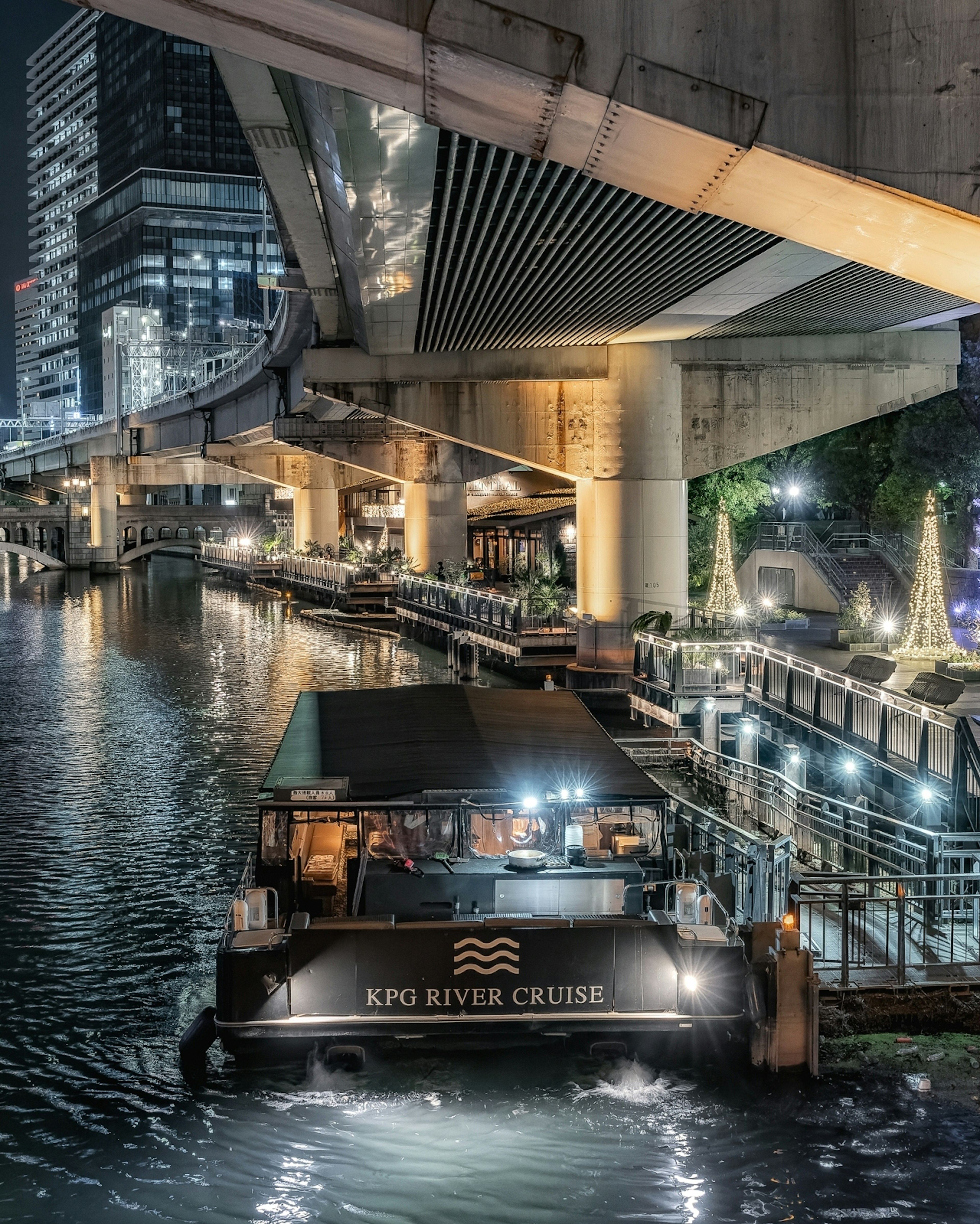 Pemandangan malam kapal pesiar sungai di bawah jembatan dengan gedung pencakar langit